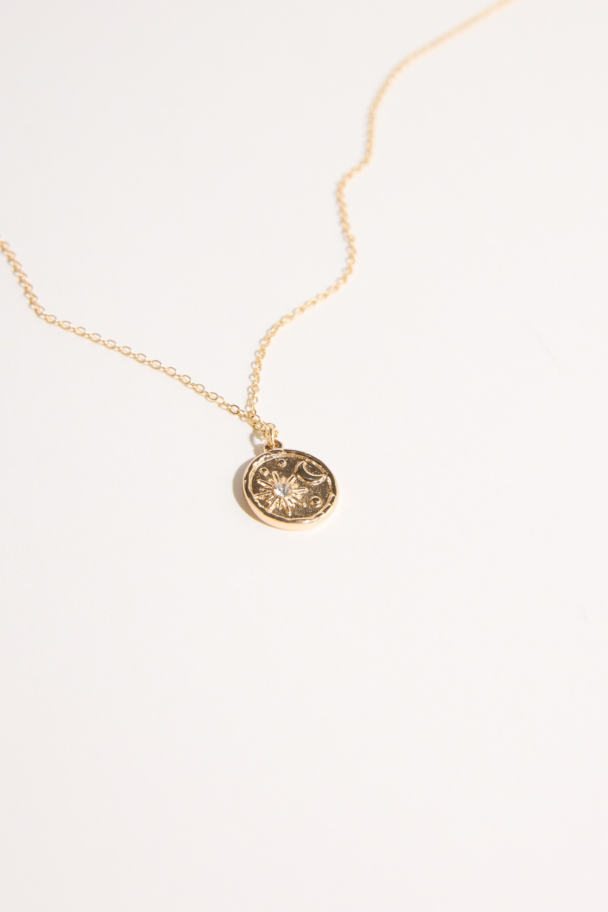 The Bela Sonder Celestina Pendant Necklace by Bela Sonder features a thin gold chain and a round, textured pendant with a star-like design, shown against a plain light background.