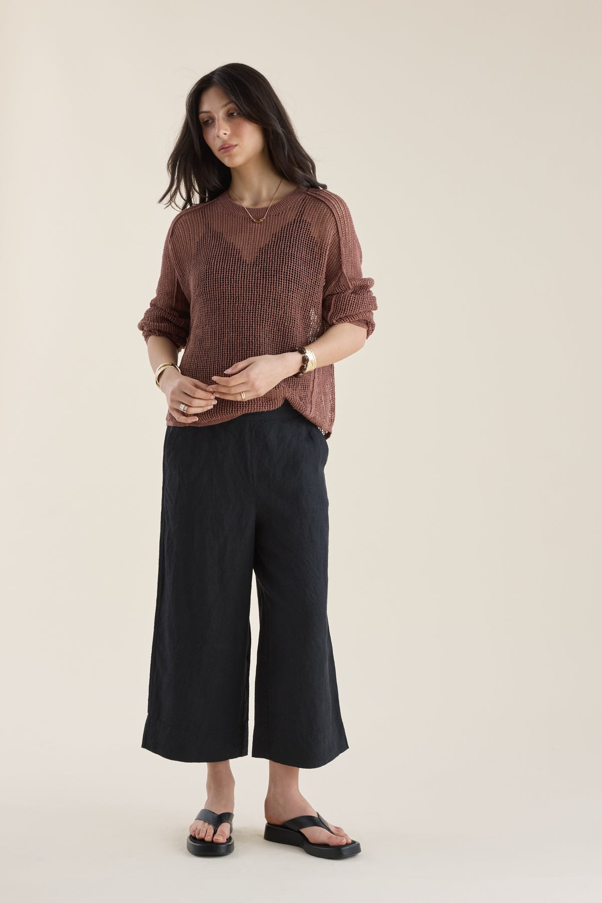 Woman in brown long-sleeve top, Elementary High Tide Linen Crop Pants, and sandals on tan floor.