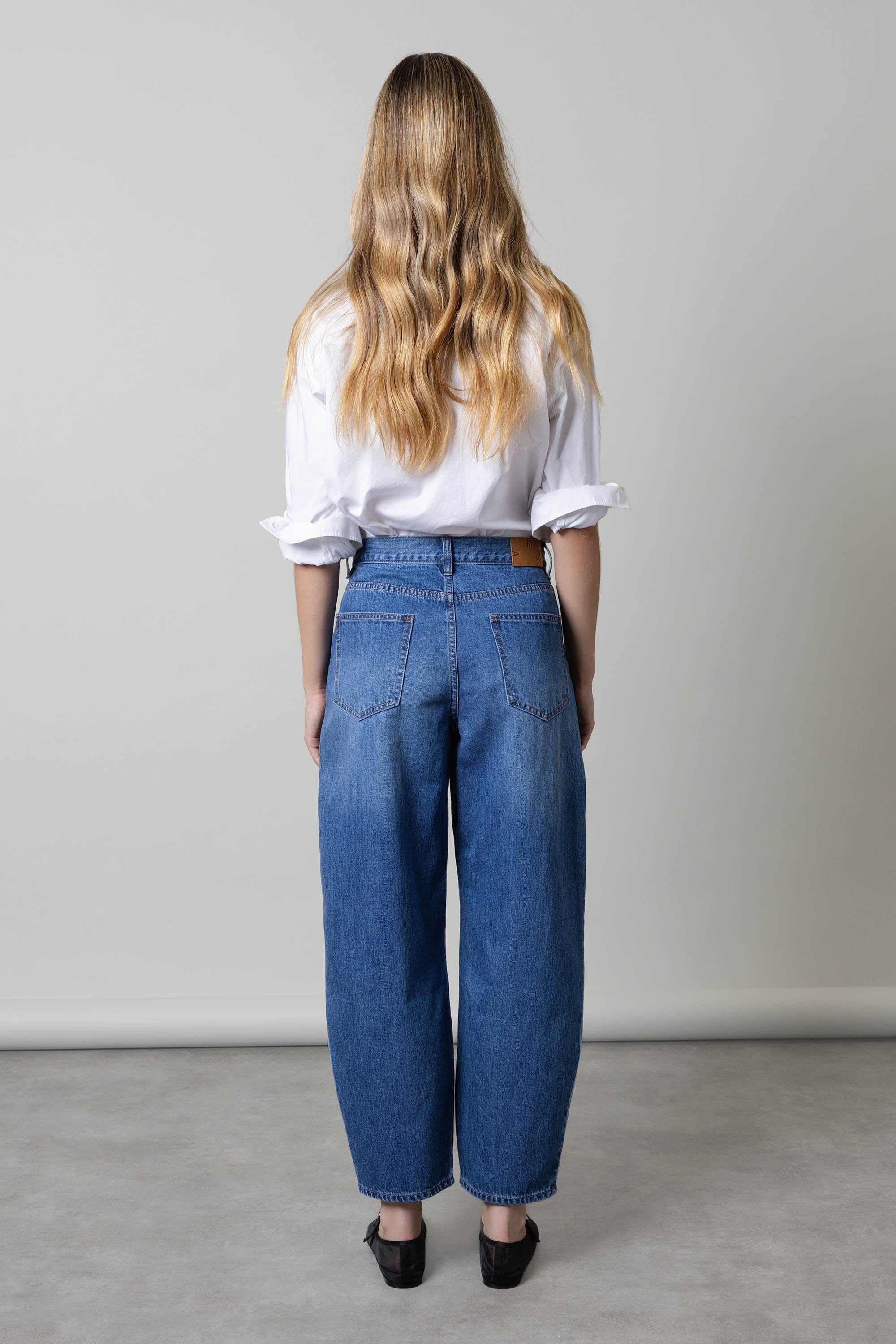 Woman in white shirt and Max Montreal Barrel Leg Jeans, back to camera, long wavy hair.