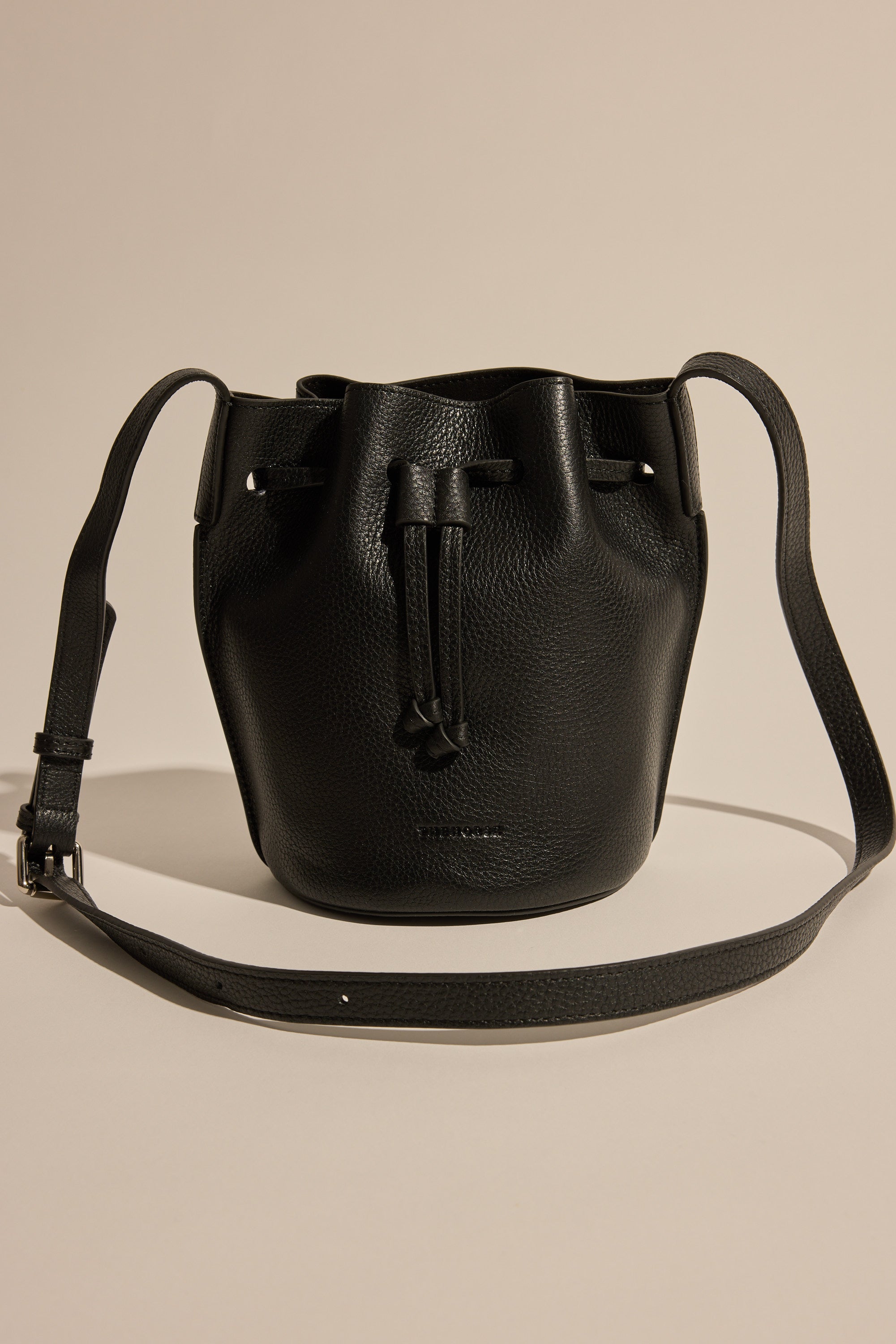 The Horse Bob Bucket by The Horse is a black grained leather bucket bag with a long adjustable crossbody strap, drawstring closure, and subtle textured finish, shown upright against a neutral background.