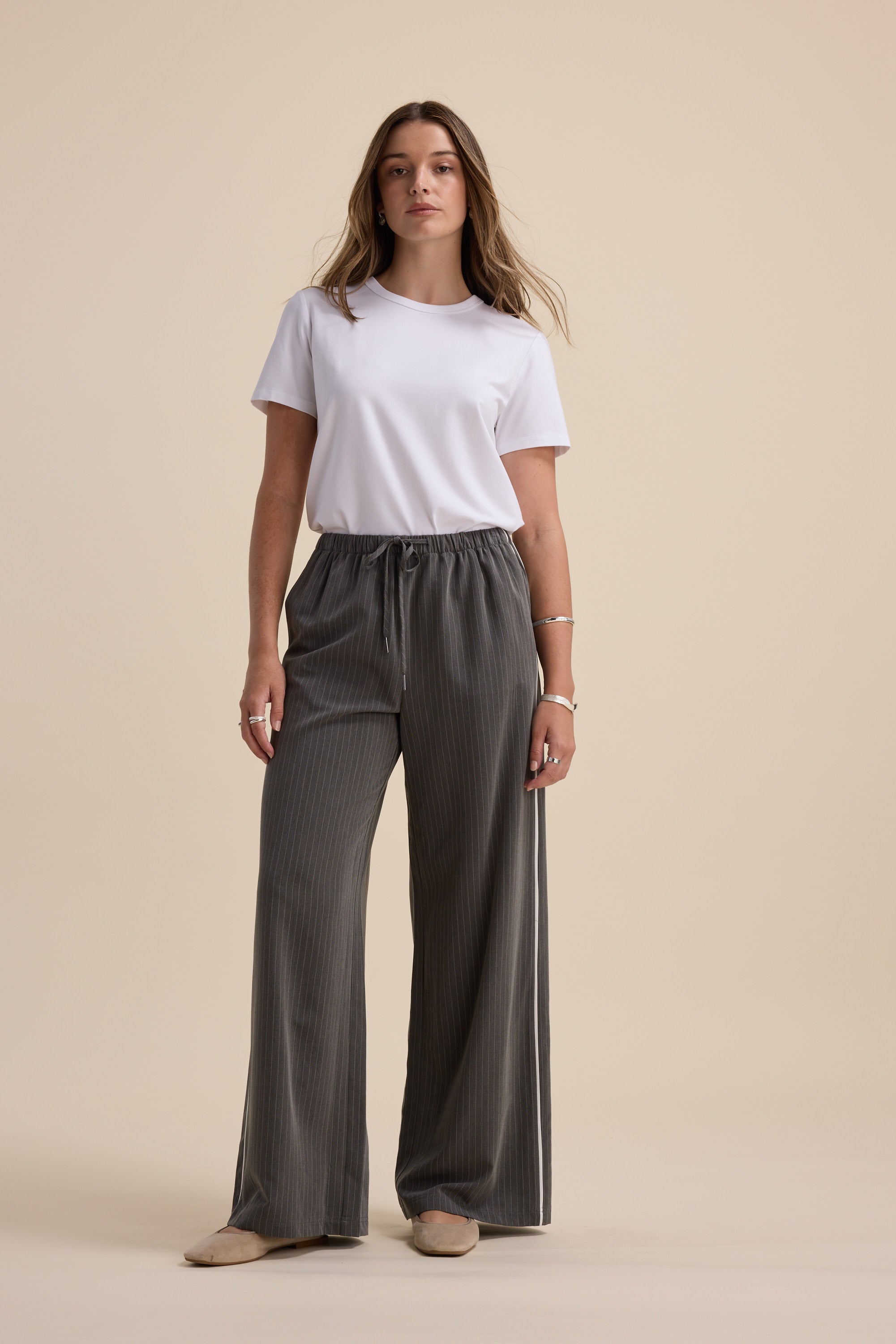 Woman wears Max’s The Elevated Jogger in gray and a white tee, posed against a beige backdrop.