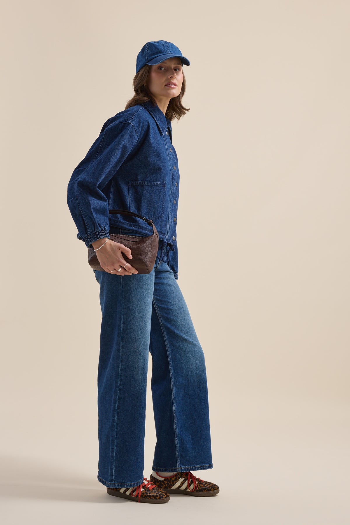 Woman in Elementary Relaxed Jacket, jeans, blue cap, with bag, on a beige background.