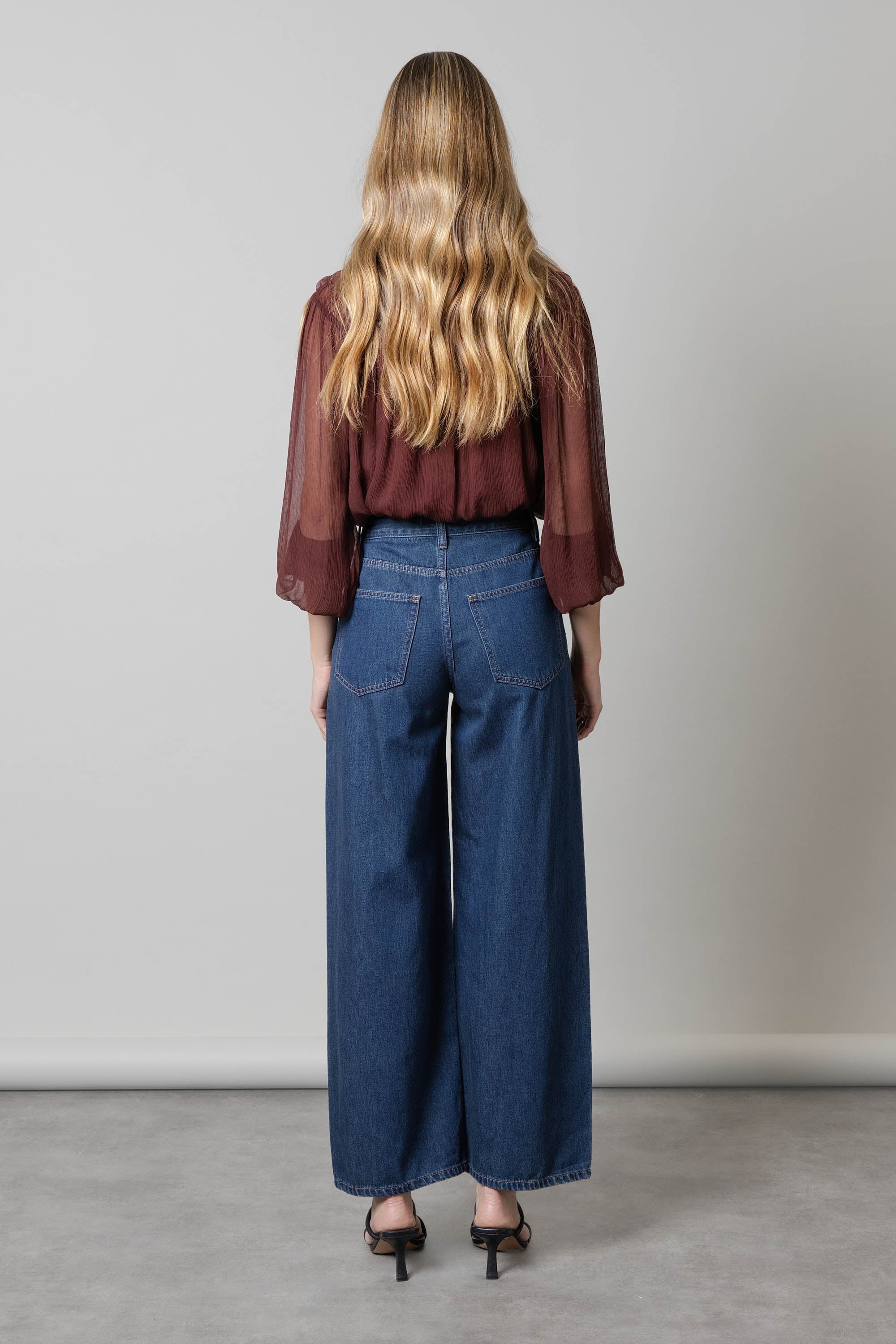 Woman in sheer maroon top and Max Aspen Wide Leg Jeans, seen from the back.