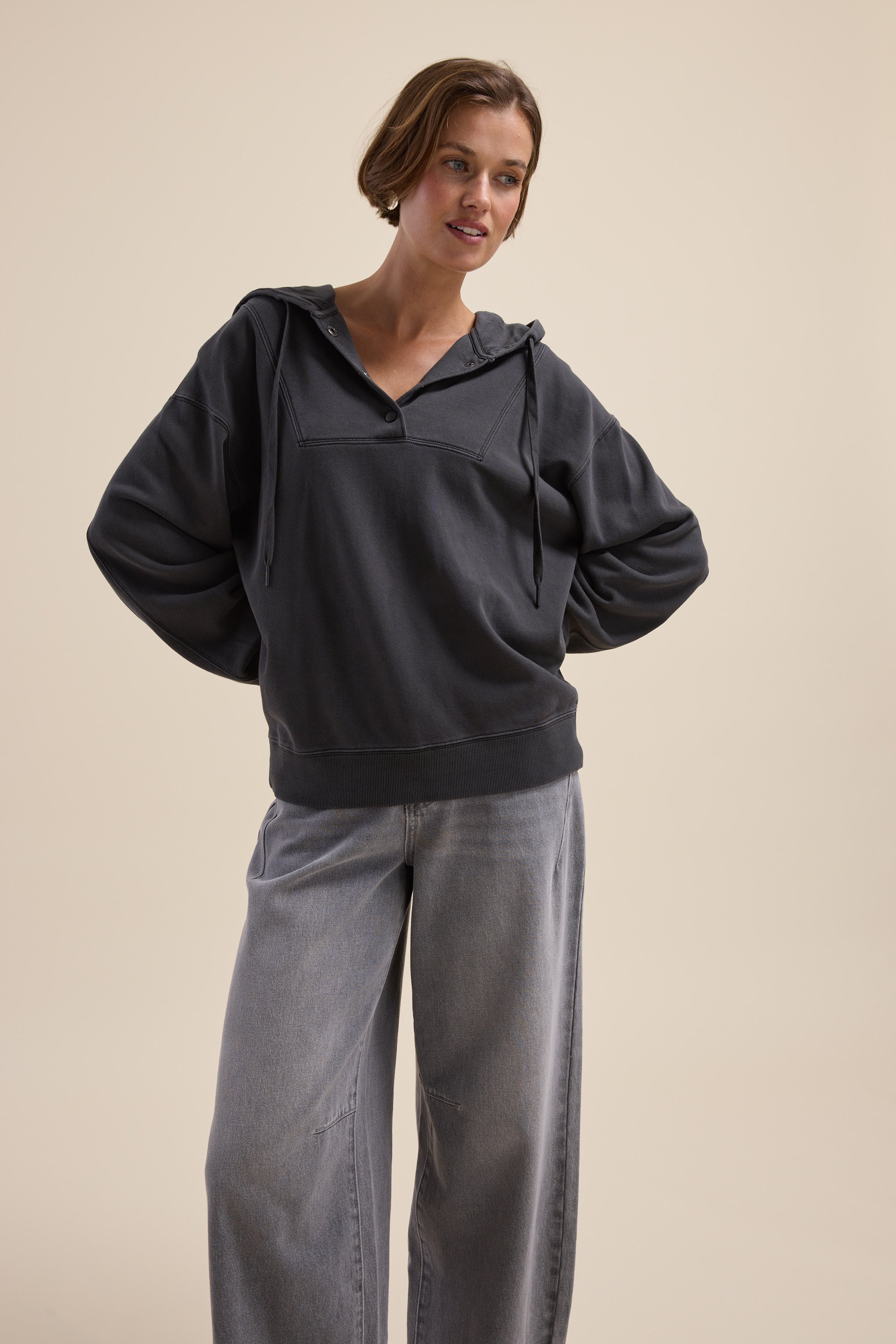 Woman in an Elementary Henley Hoodie and wide-leg jeans stands with hands behind her back.