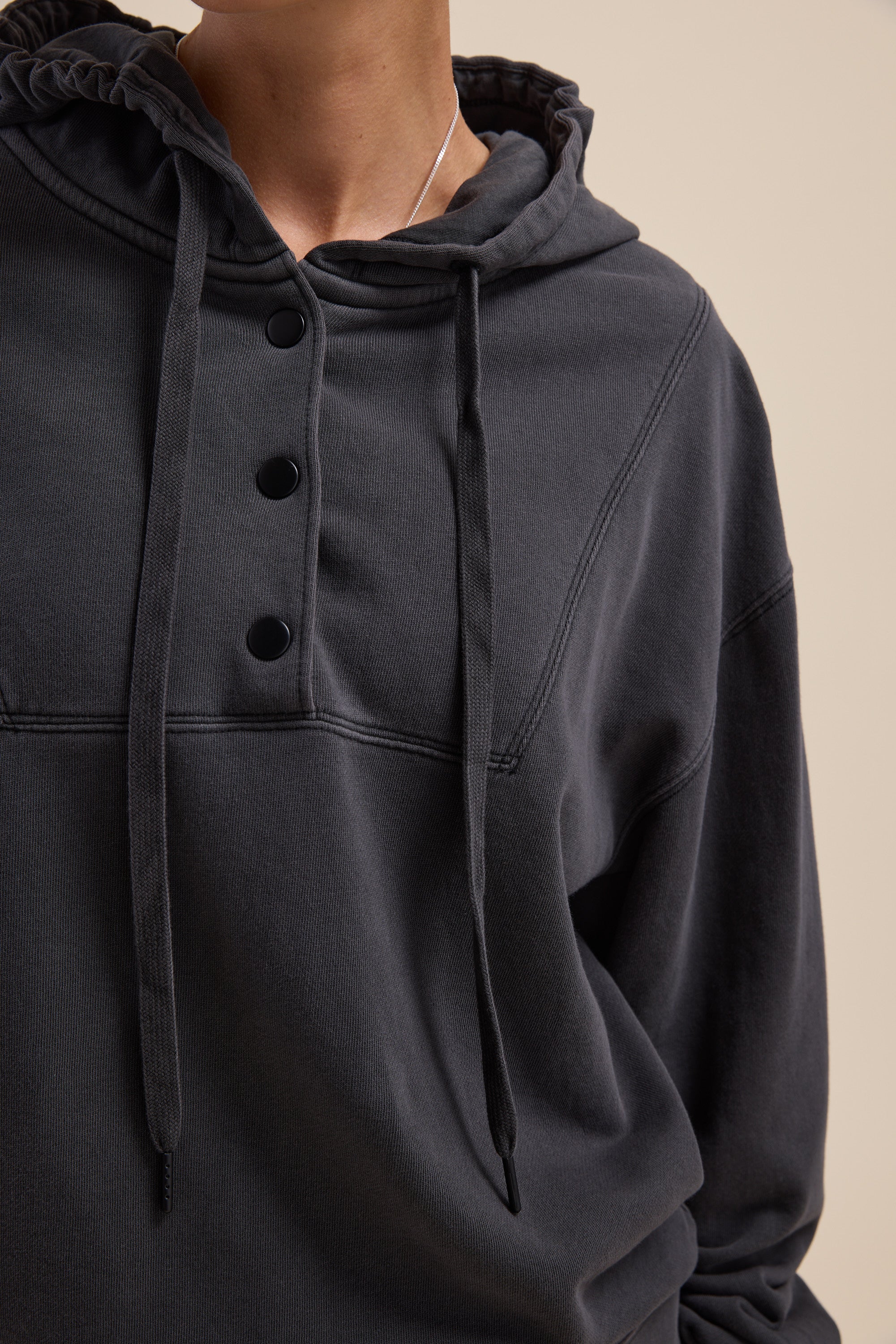 Person in a relaxed fit, dark Elementary Henley Hoodie with drawstrings; neutral background.