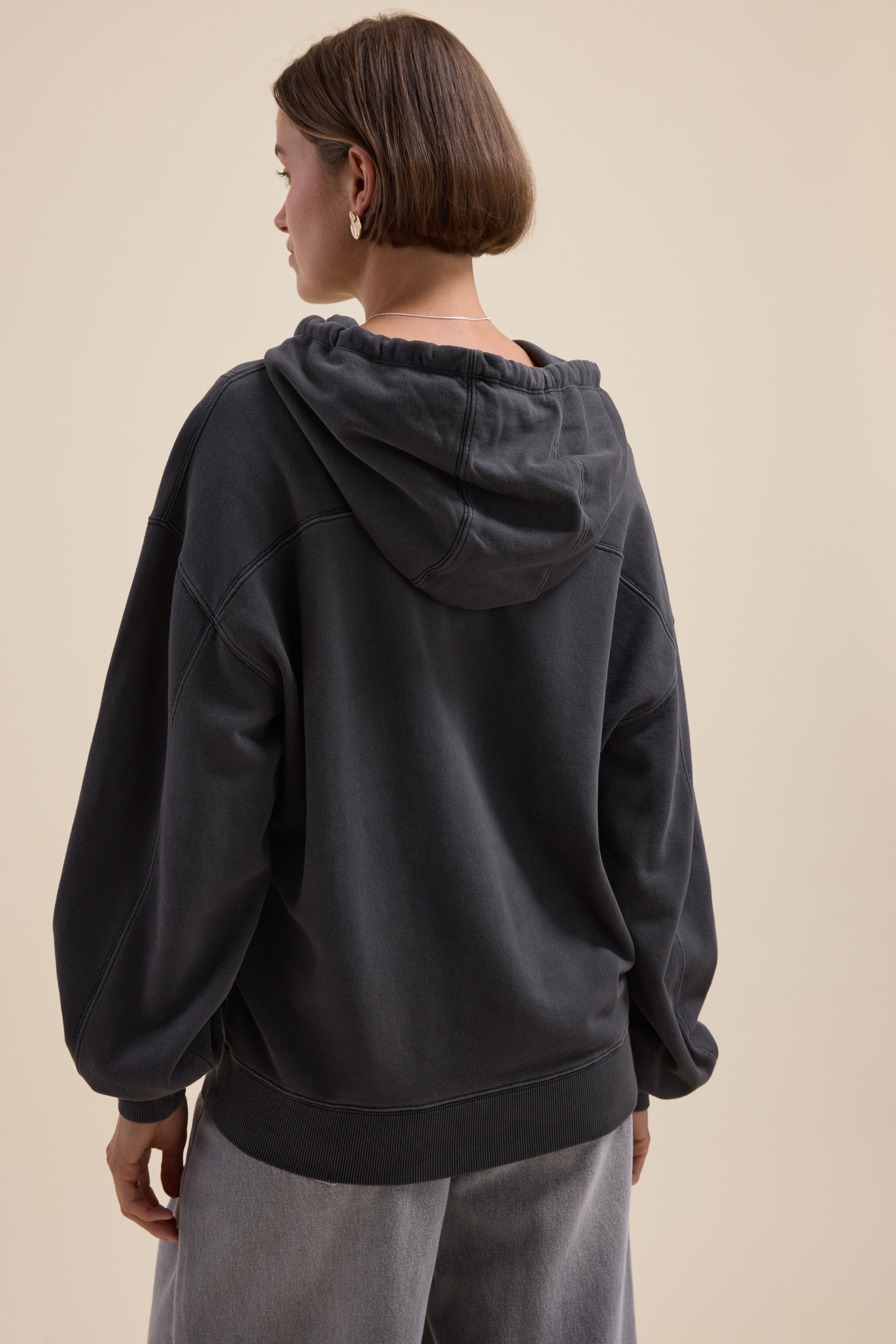 Woman in an Elementary Henley Hoodie and gray pants, back facing the camera.