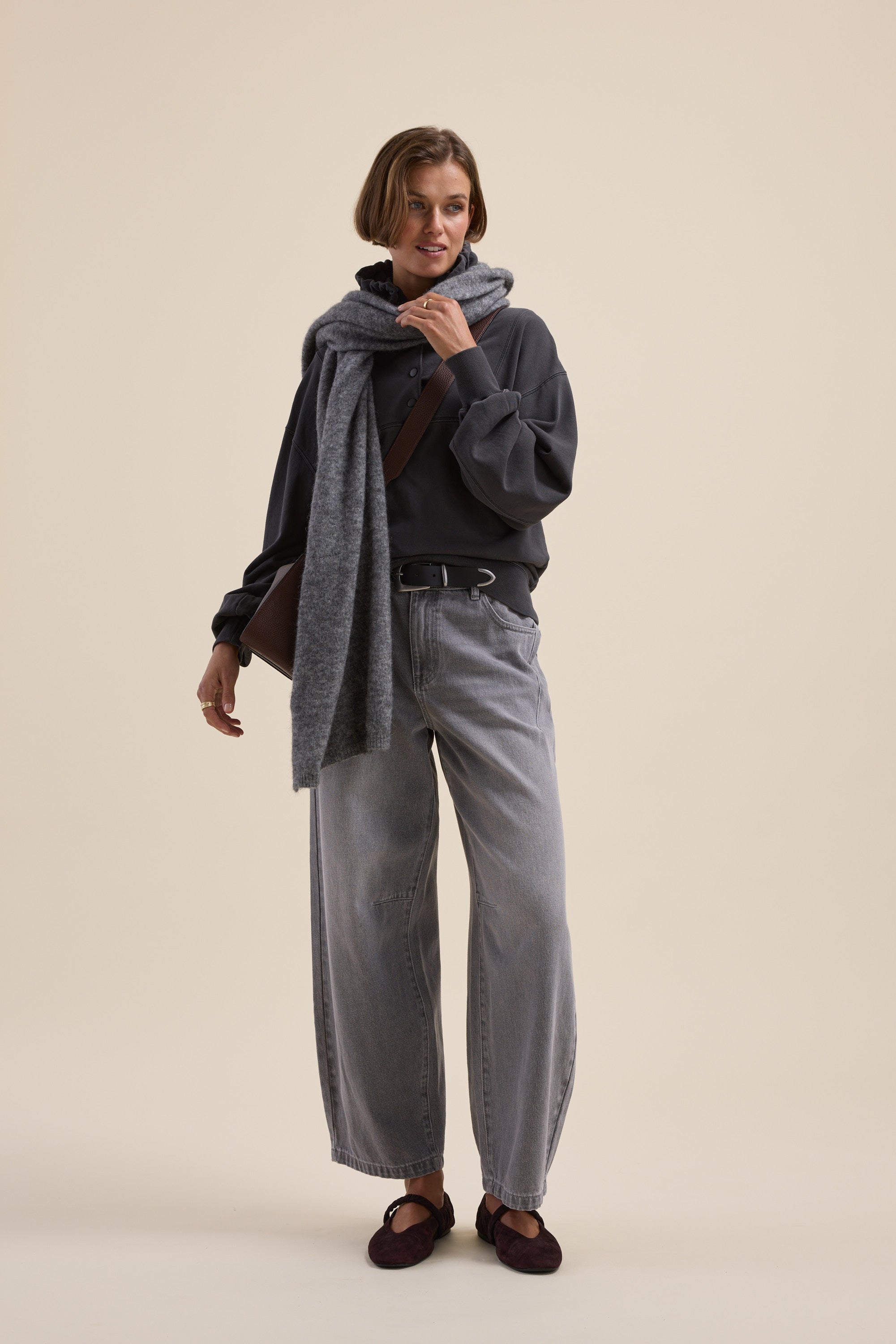 Woman in Elementary Henley Hoodie poses stylishly in wide-leg jeans, loafers, and a grey scarf.