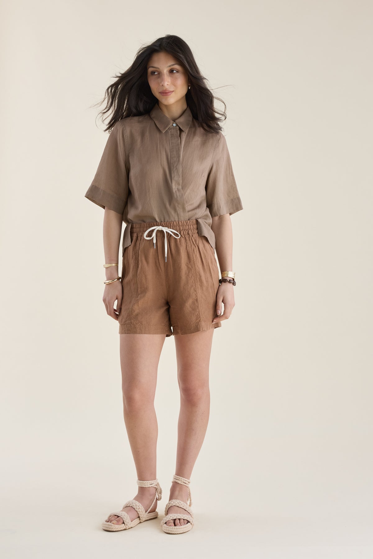 Woman in Elementary Linen Shorts and sandals, standing against a plain background.