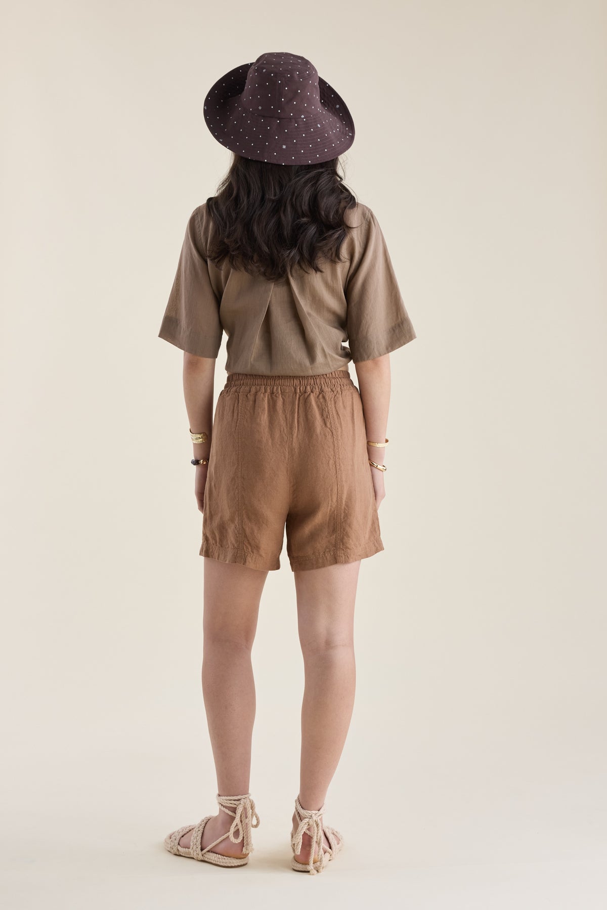 Woman in brown outfit wears Elementary Linen Short, standing with back to camera.