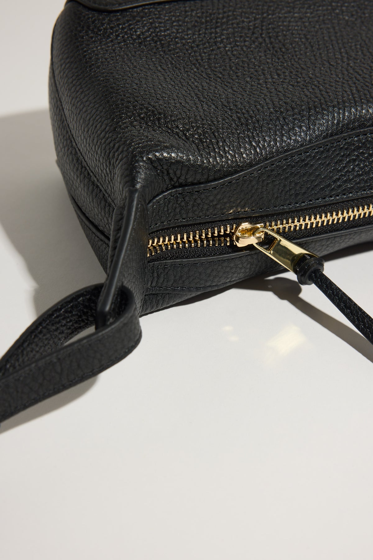 The Horse Mini Lou Bag: black pebble leather, gold zip, adjustable strap on white surface.