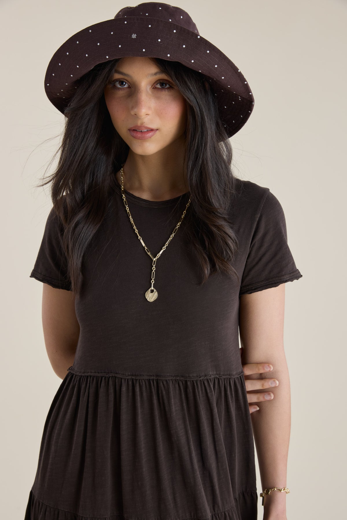 Woman in Elementary Jersey Tiered Dress, brown, with hat, gold chain necklace.