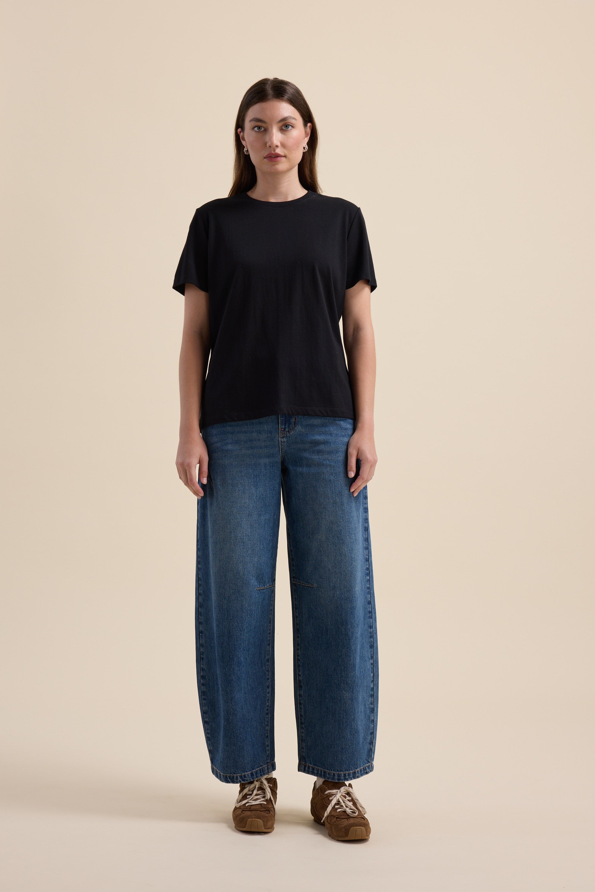 Woman in Max The Good Earth Cotton Crew Tee, wide-leg jeans, and brown shoes on beige background.