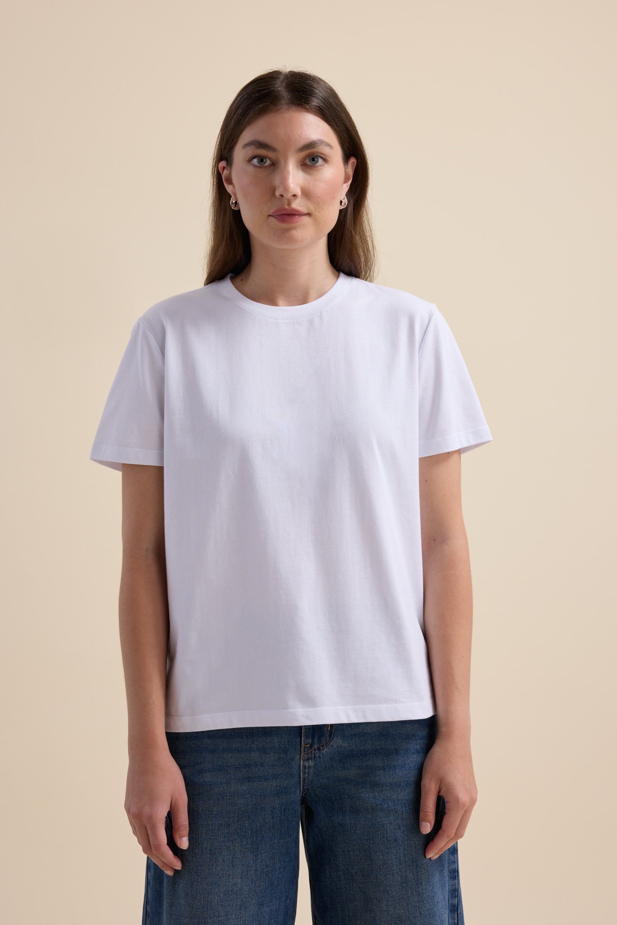 Woman in The Good Earth Cotton Crew Tee by Max and blue jeans, against a beige background.