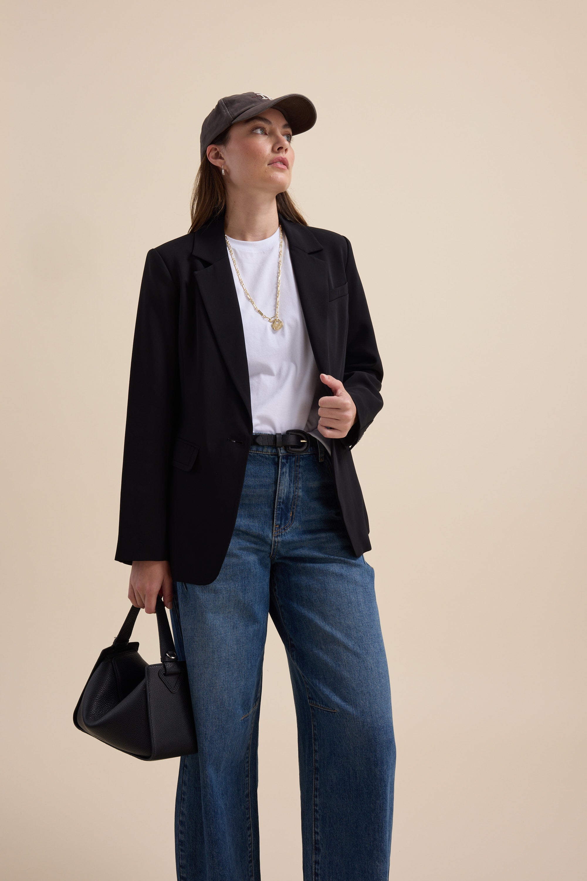 Woman in Max's The Good Earth Cotton Crew Tee, blazer, jeans, cap, handbag, looking sideways.