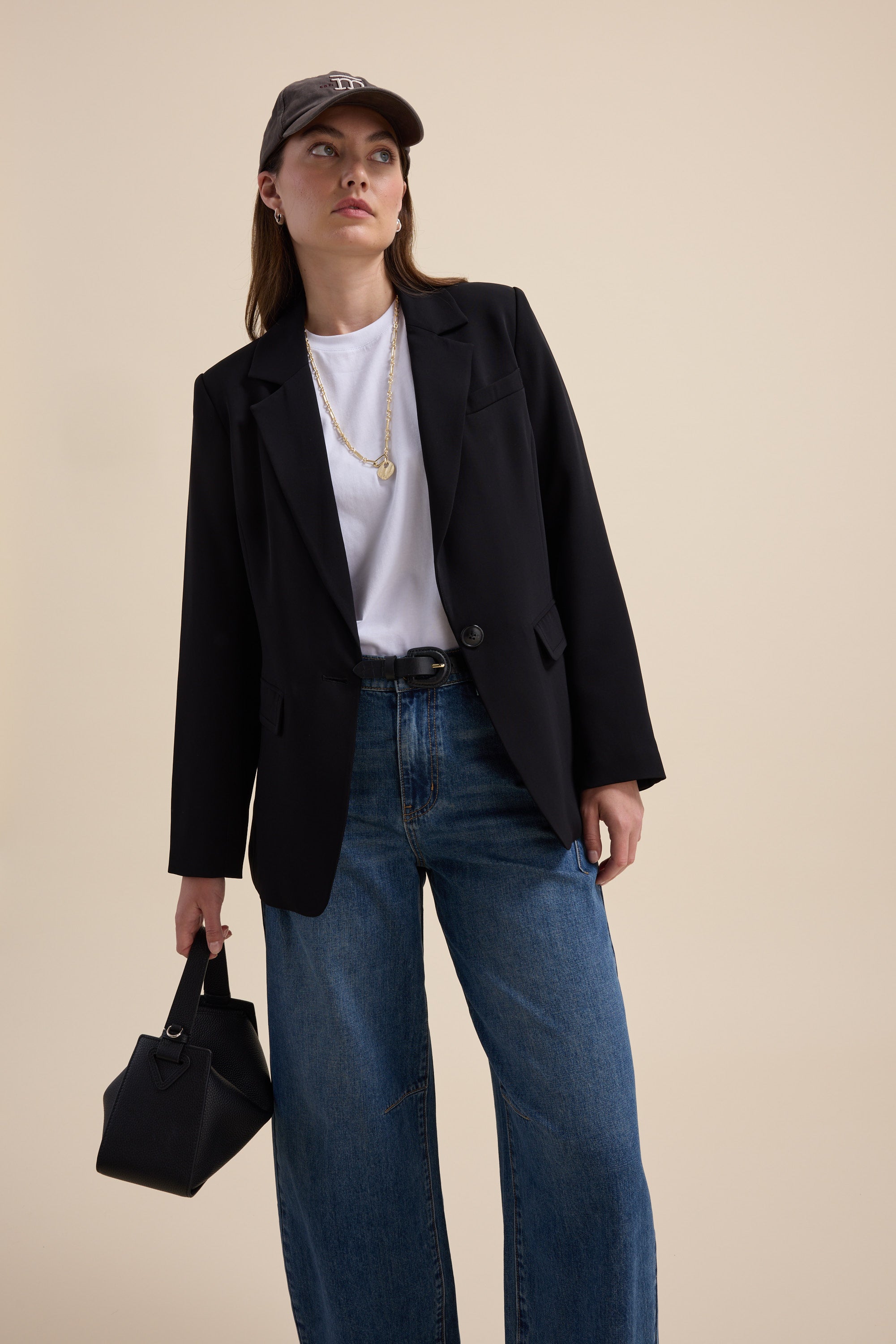 Woman in Max’s The All Occasion Blazer and jeans, holding a small black handbag.