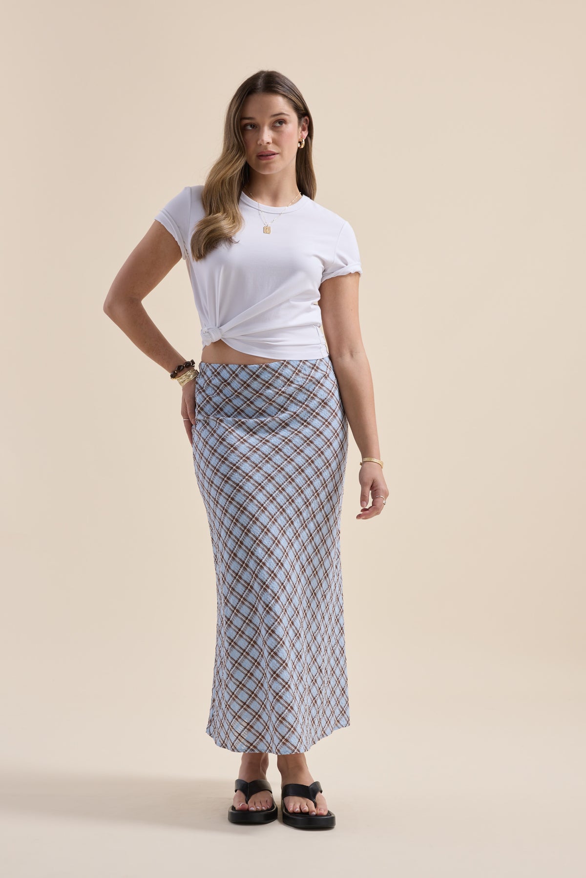 Woman in Max The Perfect Slip Skirt, white tee, and sandals against a beige background.