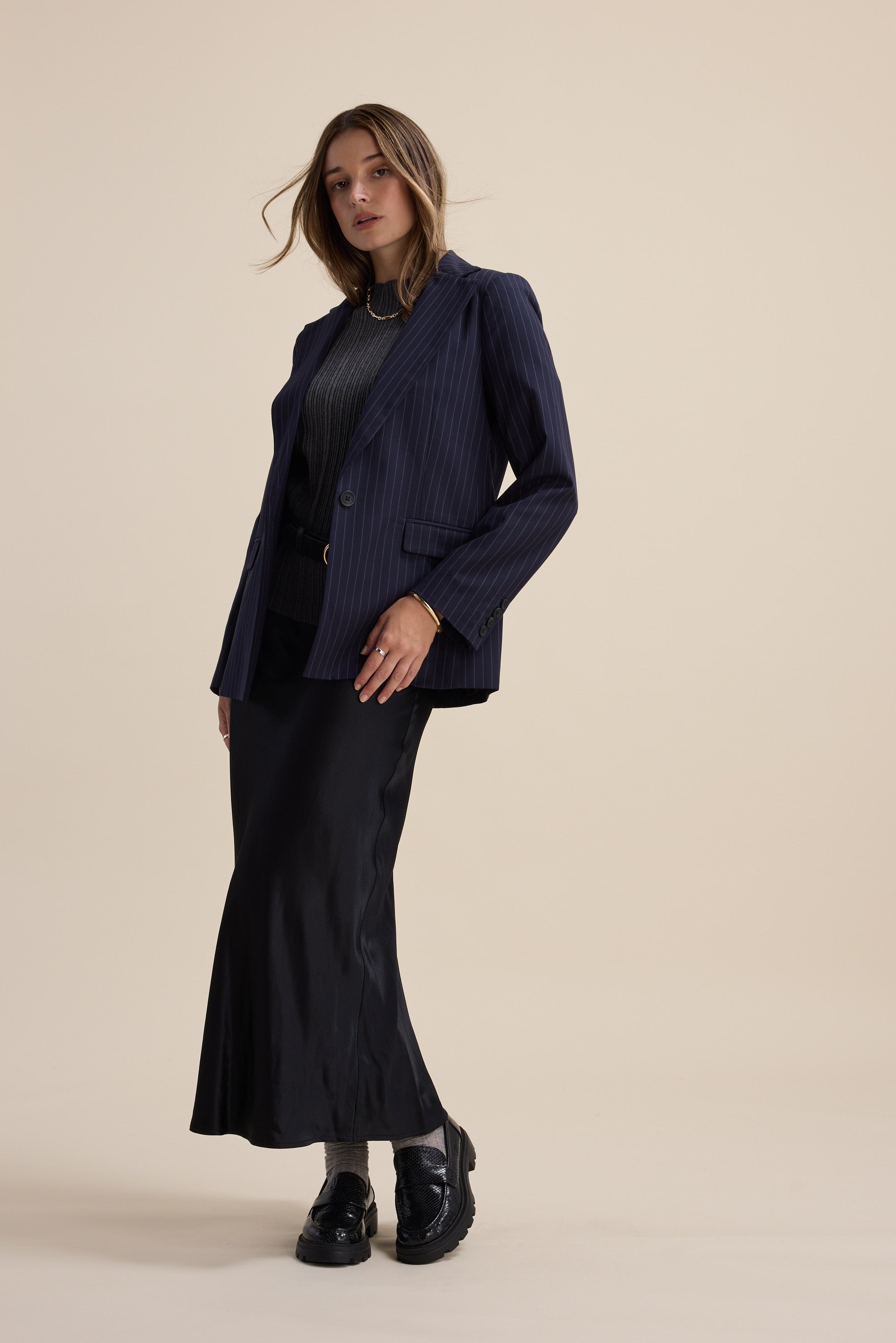 Woman in The Perfect Slip Skirt by Max and a pinstripe blazer poses against a beige background.
