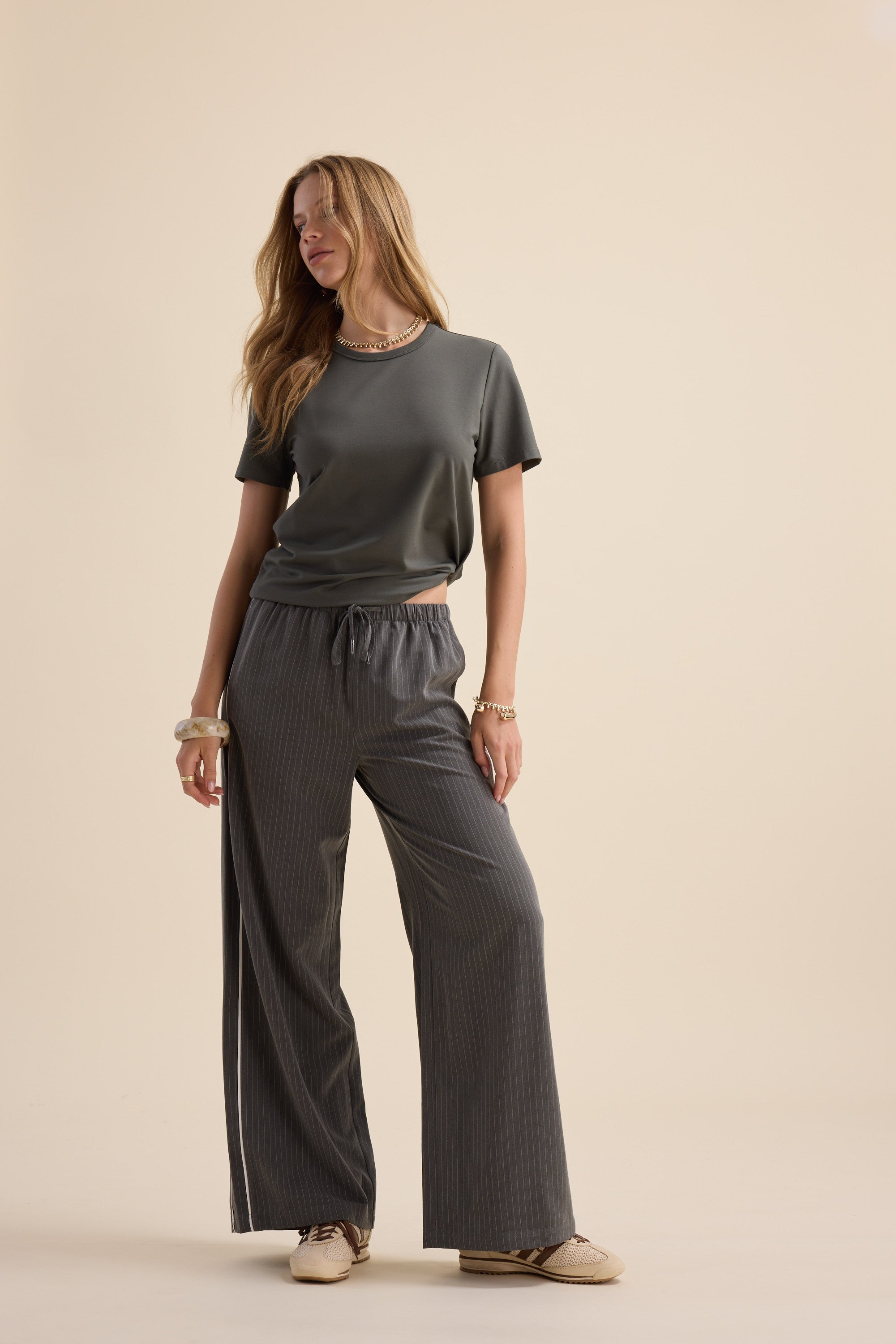 Woman in The Perfect Short Sleeve Crew Neck Tee by Max and wide-leg pinstriped pants, beige background.