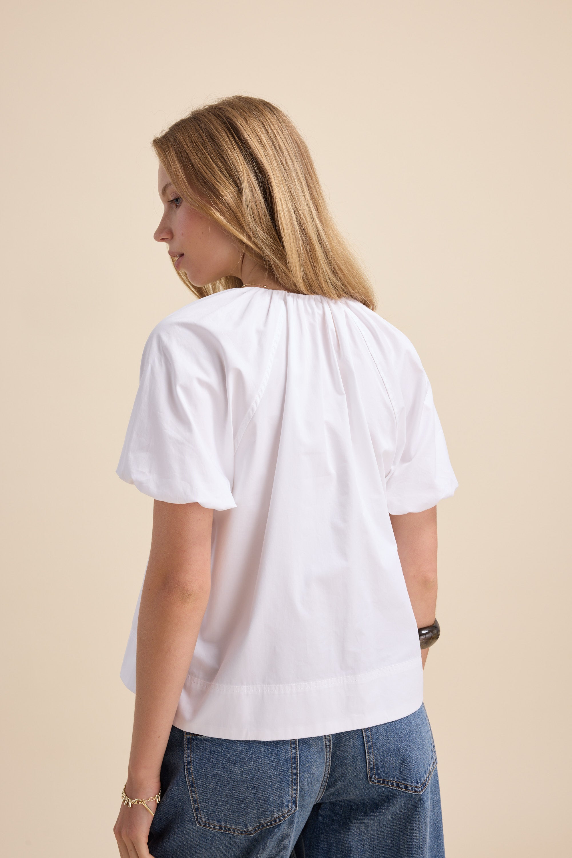 Woman wears Max's The Poplin Blouse with puff sleeves and jeans, back to the camera.