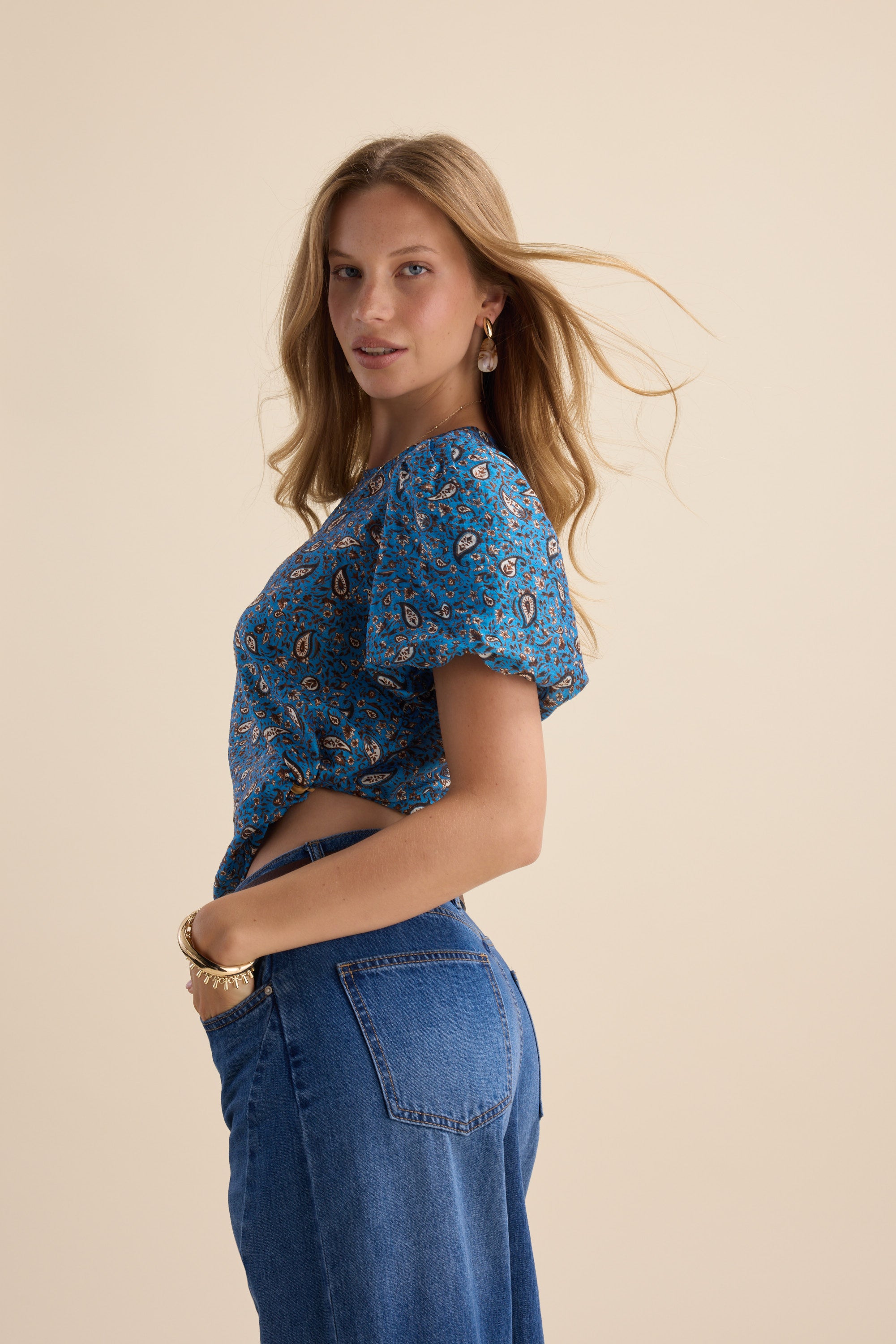 Woman in Max Sydney Back Detail Top poses sideways against a beige background.