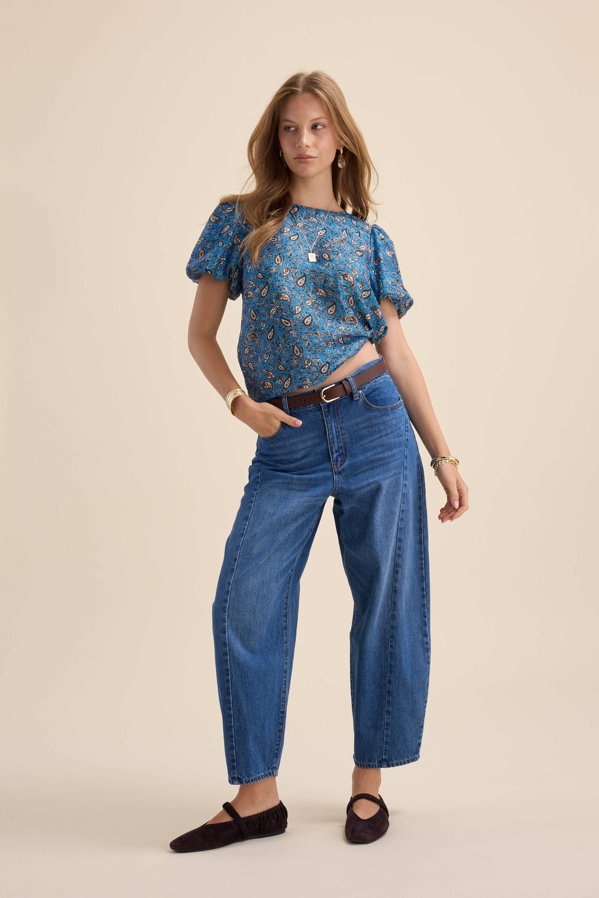 Woman wears Max Sydney Back Detail Top with blue jeans and black flats against beige background.