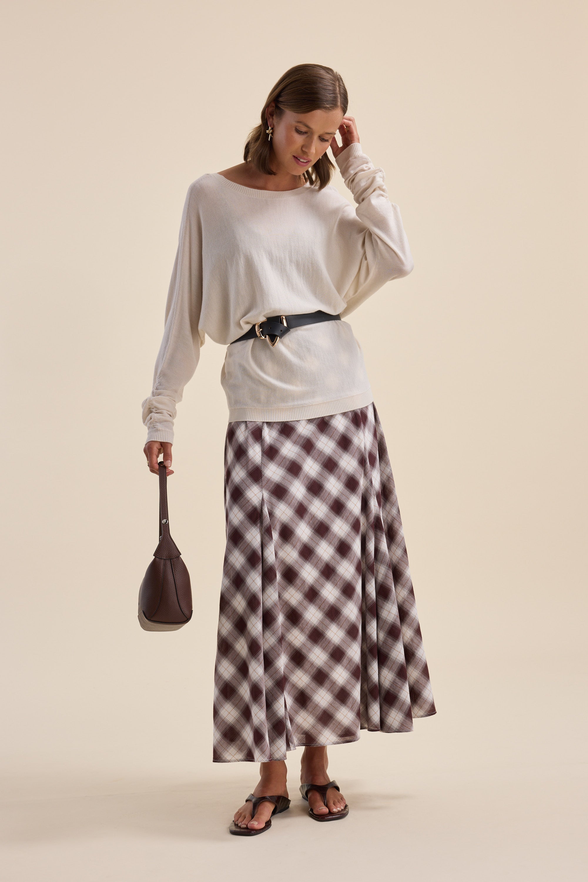 Woman in Elementary ZQ Merino Reversible Sweater, checkered skirt, black belt, brown bag, sandals.