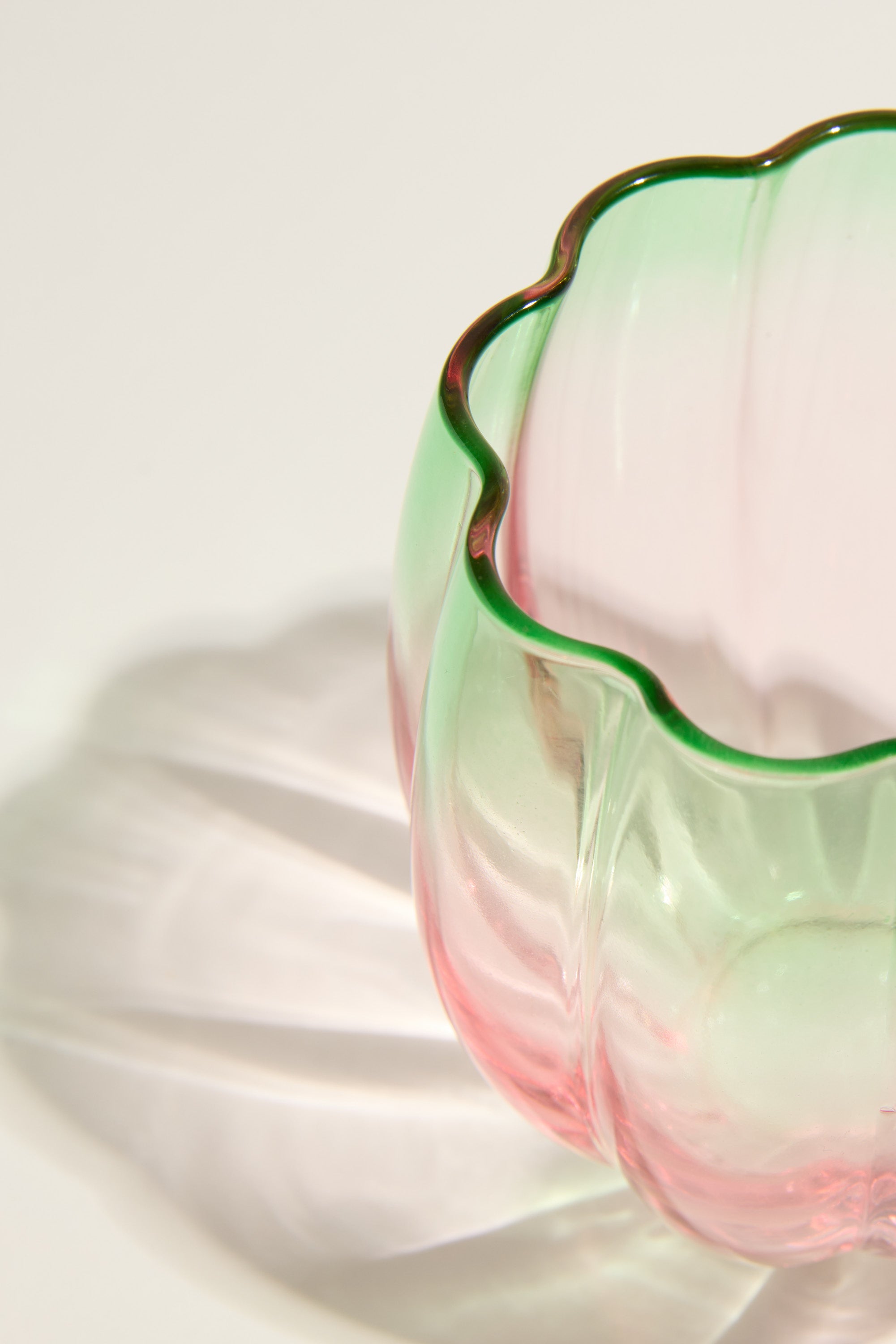 A close-up of the Homelab Petal Stemless Glass Set by Homelab, featuring pink and green hues, scalloped edges, and a wavy shadow on a white surface—showcasing truly unique glassware.