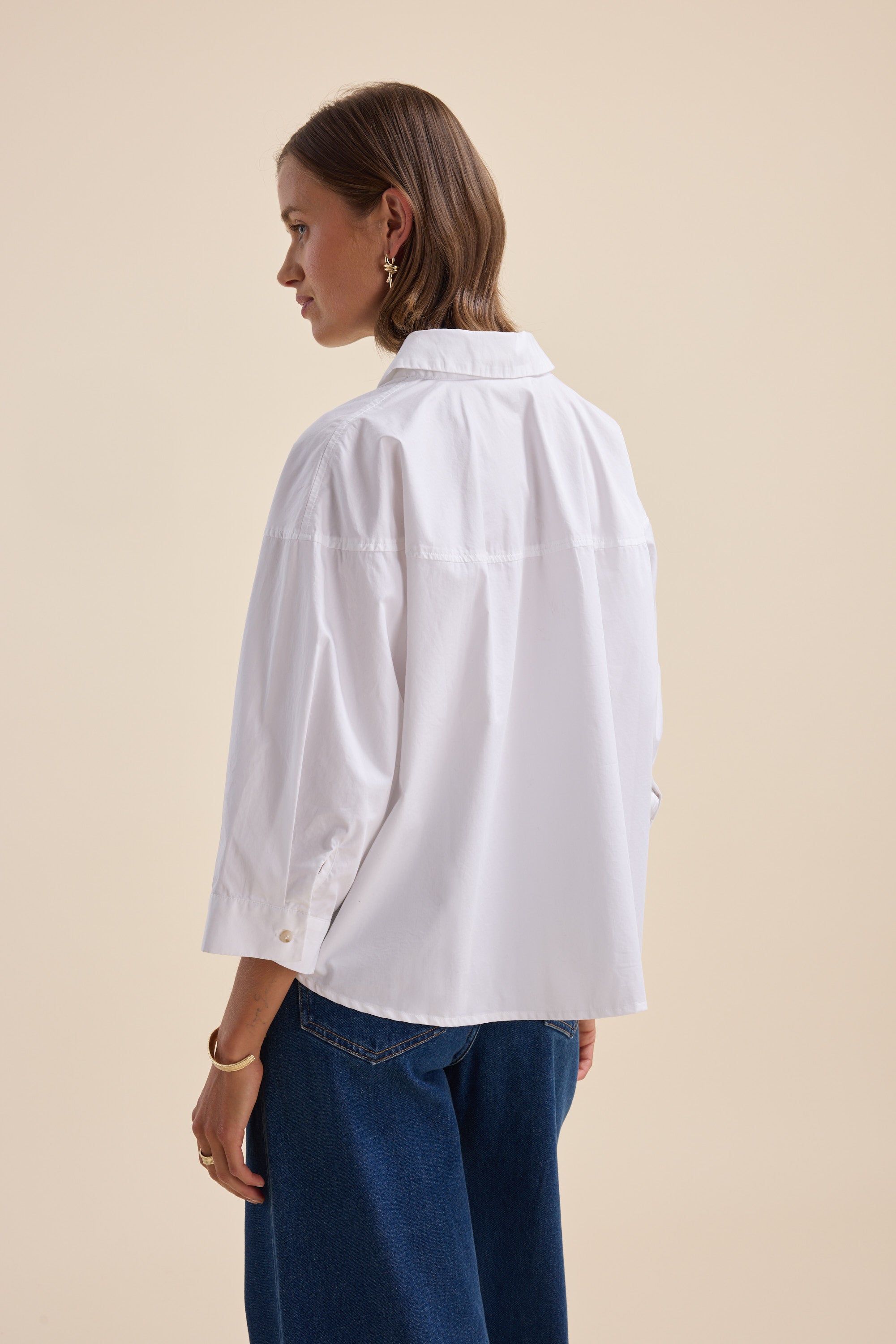 Woman in an Elementary Yoke Detail Shirt by Elementary and blue jeans, facing away.