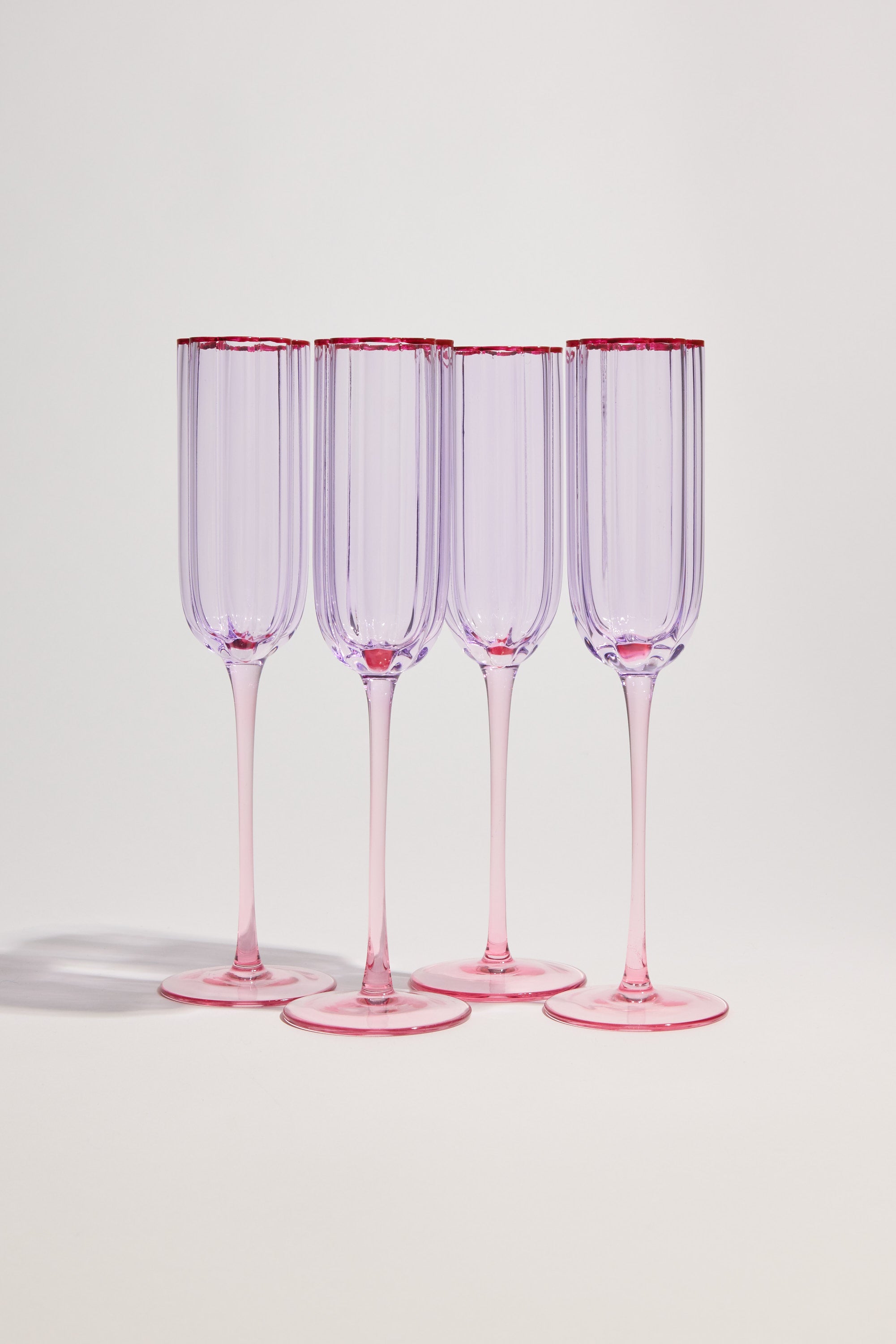 The Homelab Petal Champagne Flute Set features four clear glasses with a light purple tint and pink rims, arranged on a white surface—a stylish glassware set by Homelab for any occasion.