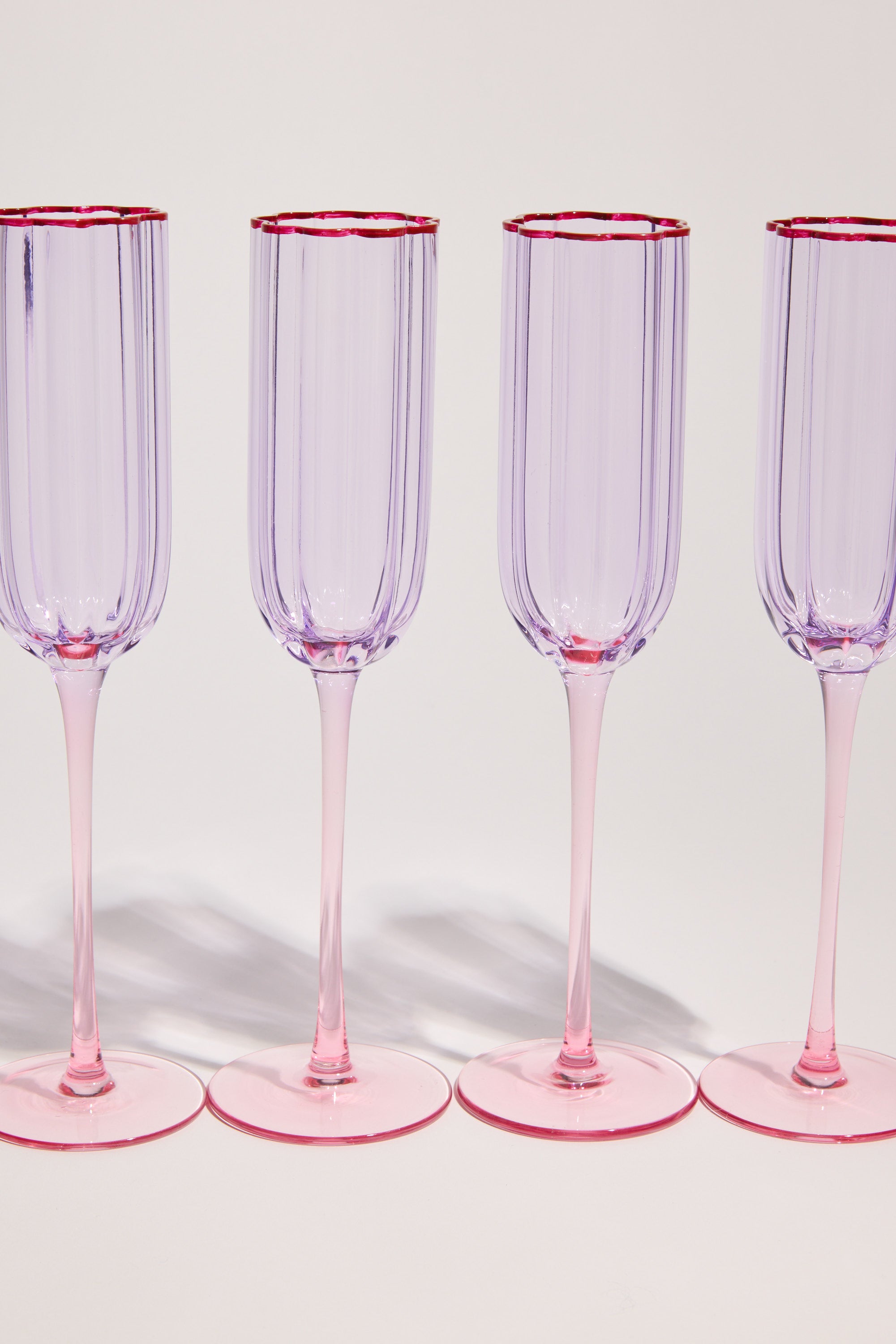 The Homelab Petal Champagne Flute Set by Homelab features elegant flutes with pink bases and rims, arranged in a row against a light background to showcase their stylish design.