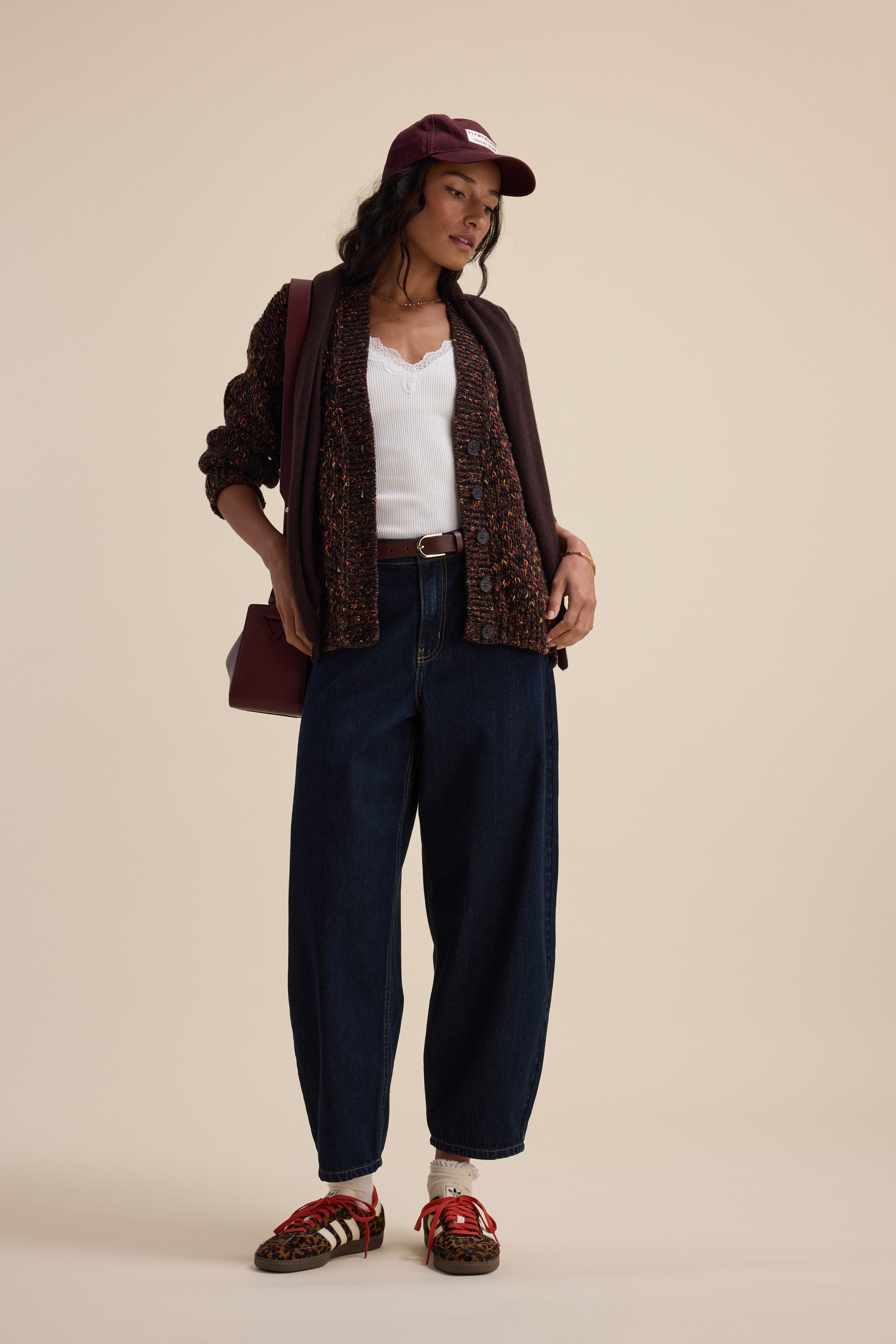 Woman in casual outfit with maroon cap, white top, jeans, sandals & Elementary cardigan.