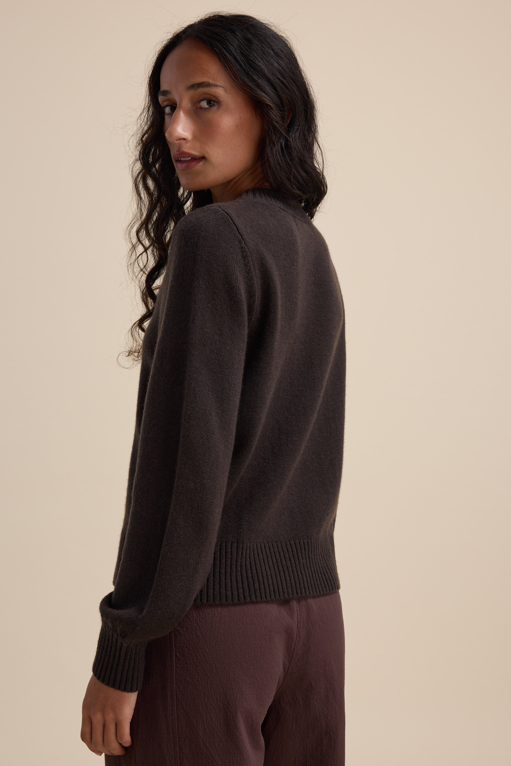Woman with long curly hair in an Elementary Cashmere Blend Crew Neck Sweater, looking back.