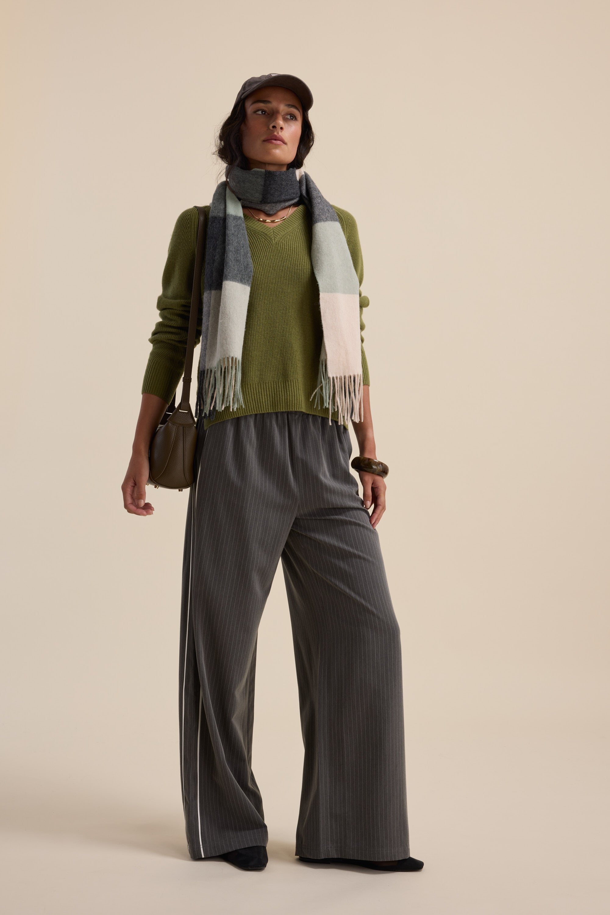 Woman in Elementary Cashmere Blend V Neck Sweater, wide gray pants, scarf, and cap.