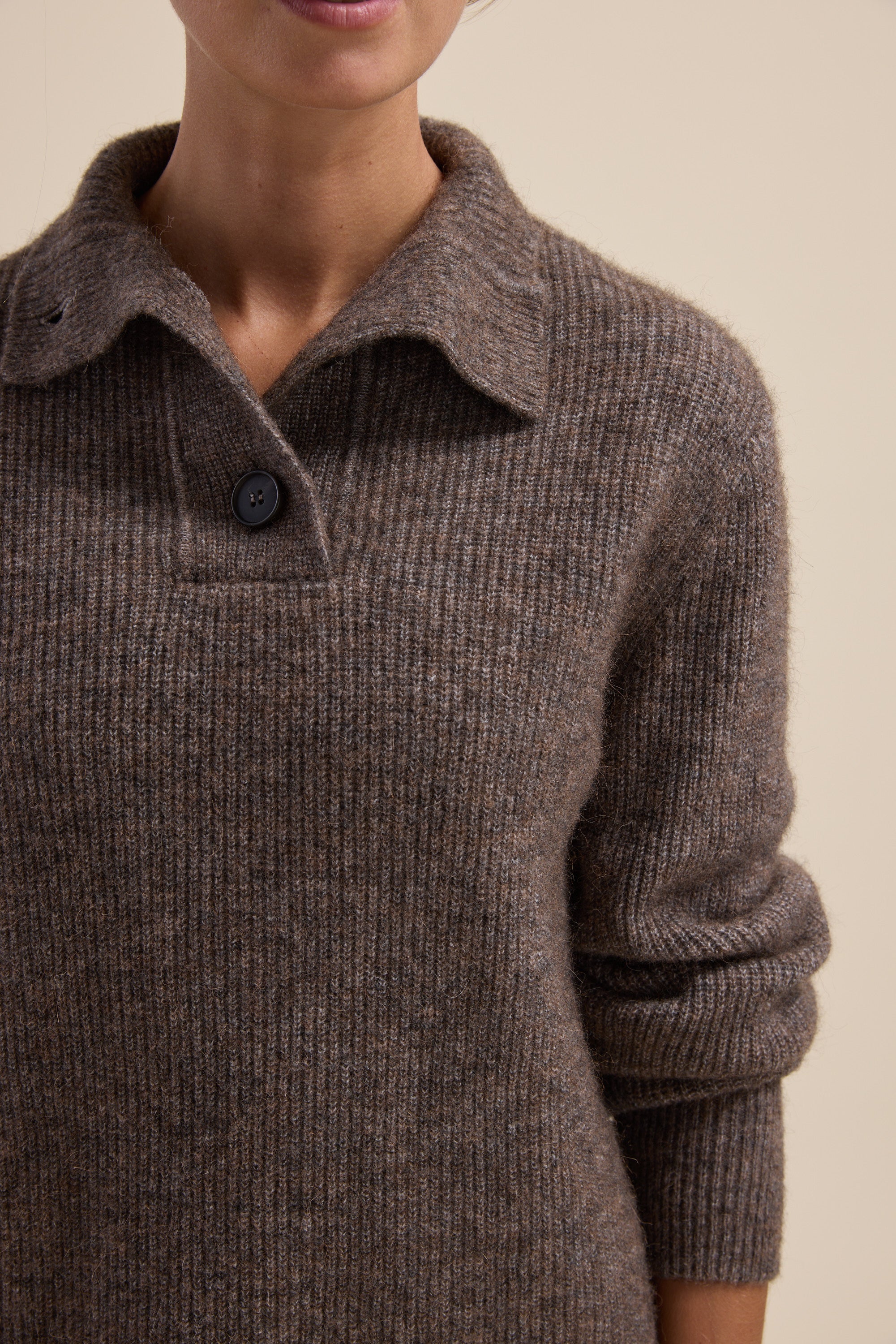 Person wearing an Elementary brown sweater with a collar detail and a single black button.