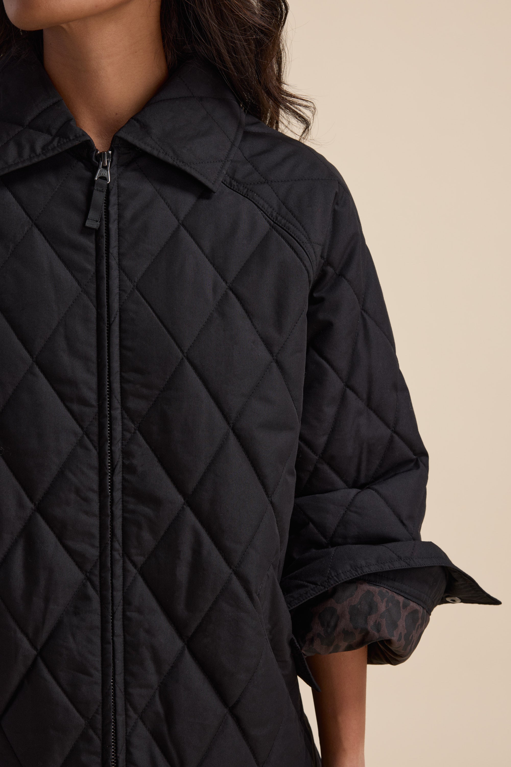 Woman wearing Elementary Quilted Puffer by Elementary, black with rolled sleeves, waist-length.