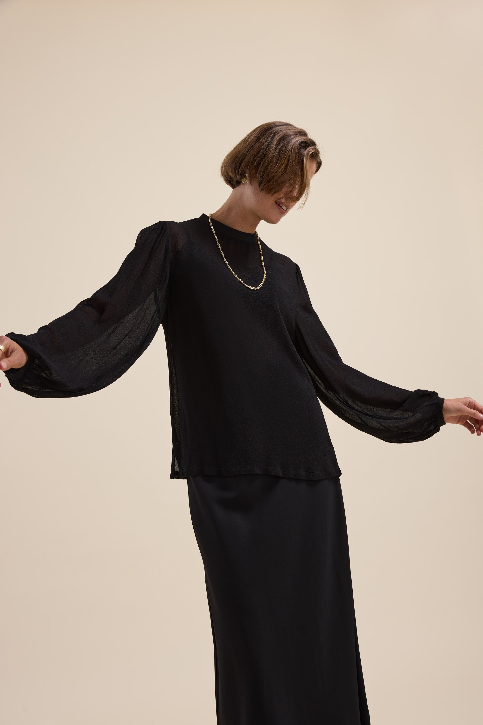 Model wears The Ultimate Layering Top by Max in black, posed against a beige background.
