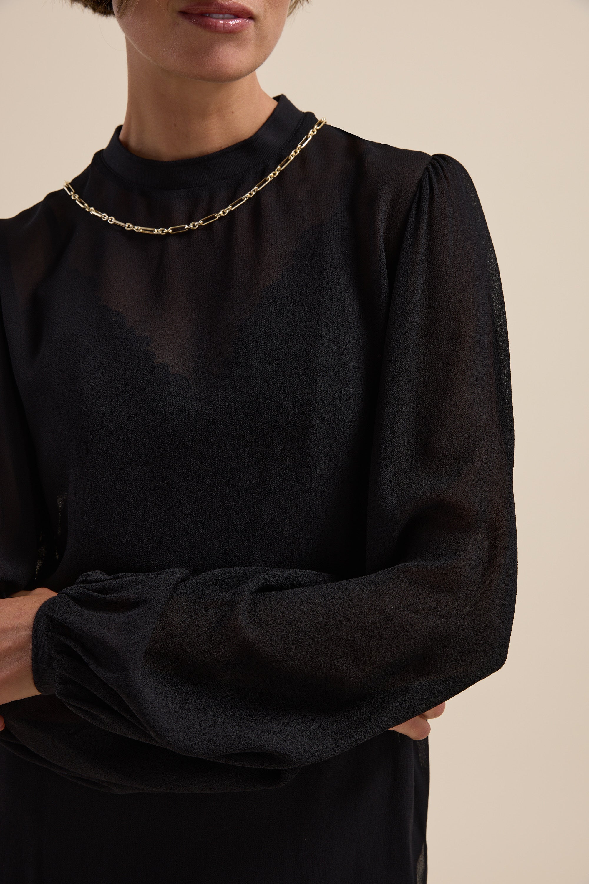Woman in Max's The Ultimate Layering Top, a sheer black blouse, arms crossed.