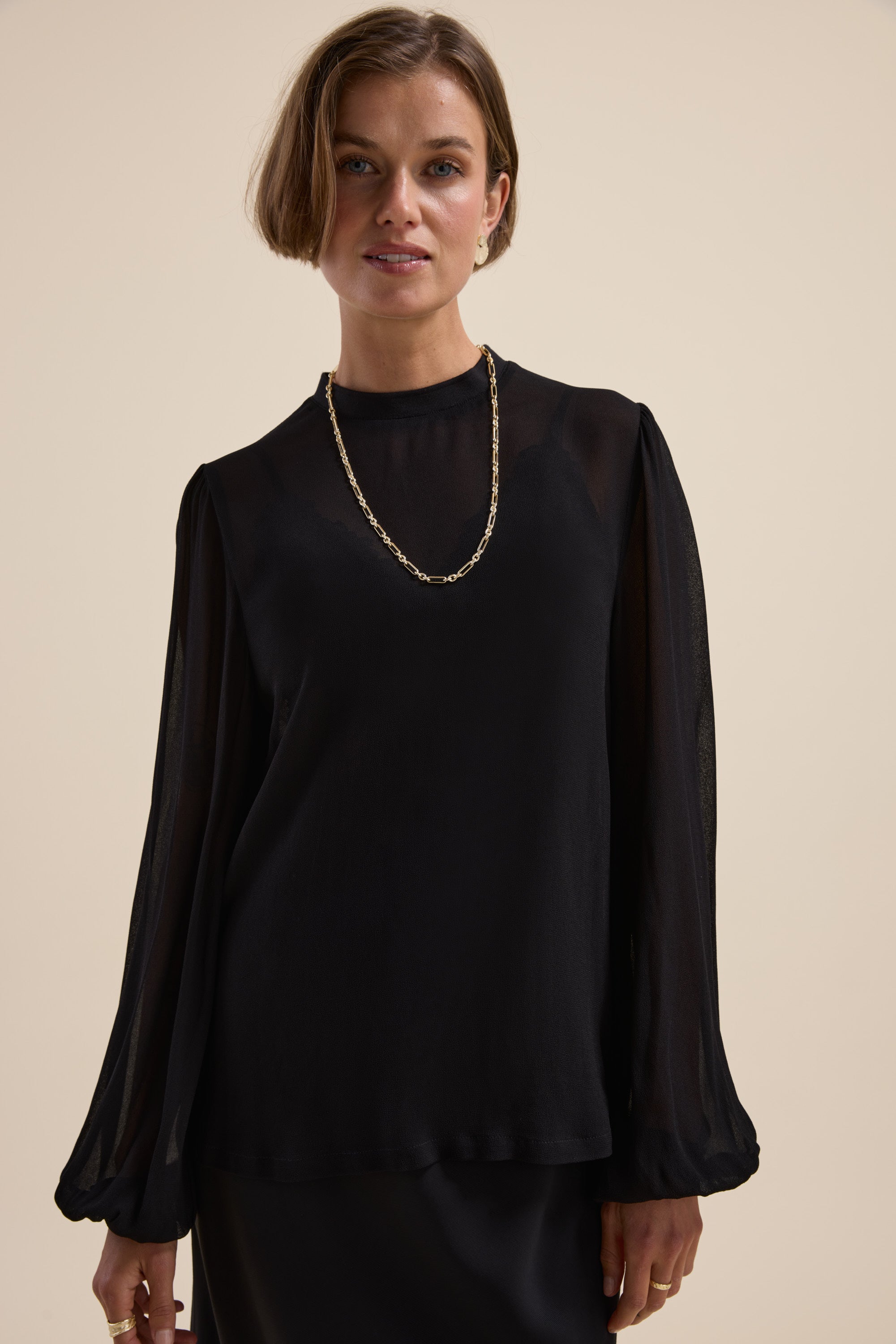 Max’s The Ultimate Layering Top in sheer black, paired with a gold chain necklace.