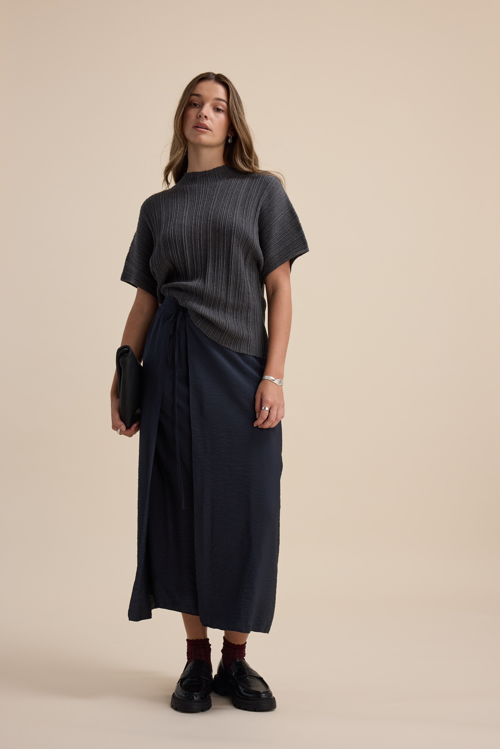 Woman in Max Briana Cotton Cashmere Ribbed Top and navy wrap skirt with a black clutch.