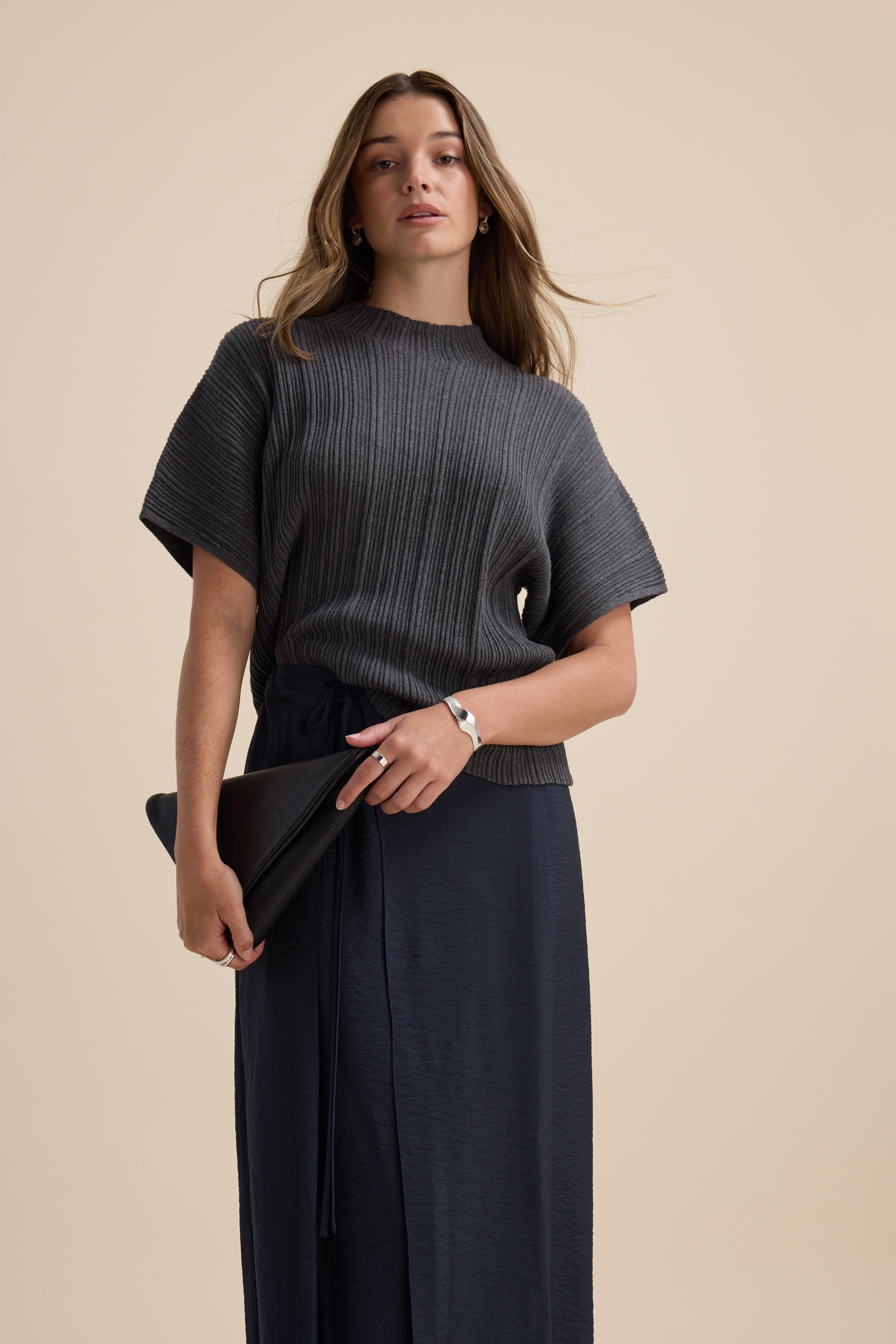 Woman in Max Briana Cotton Cashmere Ribbed Top and navy skirt, holding a black clutch.