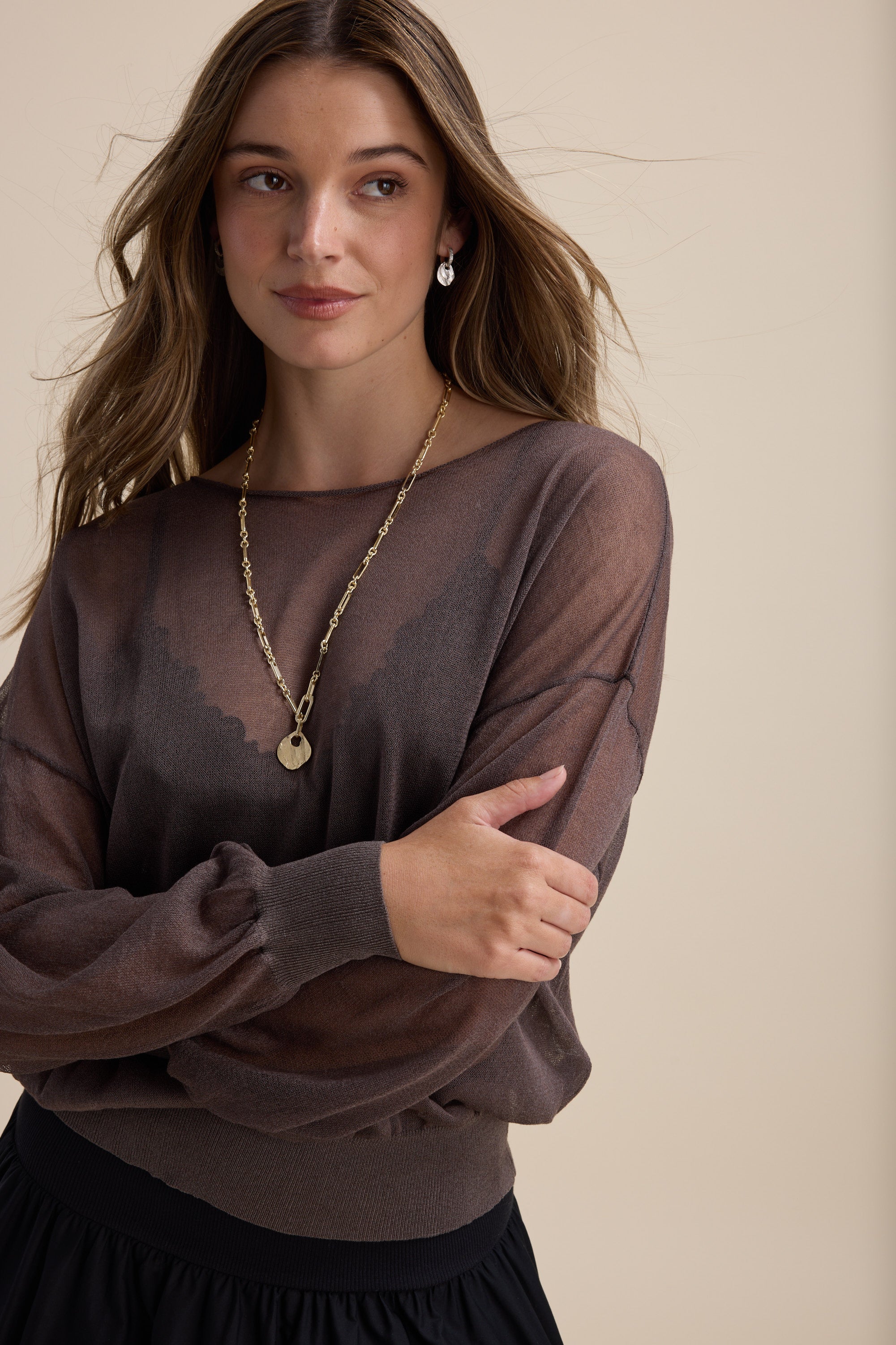 Woman with long hair in the Max Addie Sheer Knitted Top, gold necklace, and earrings.