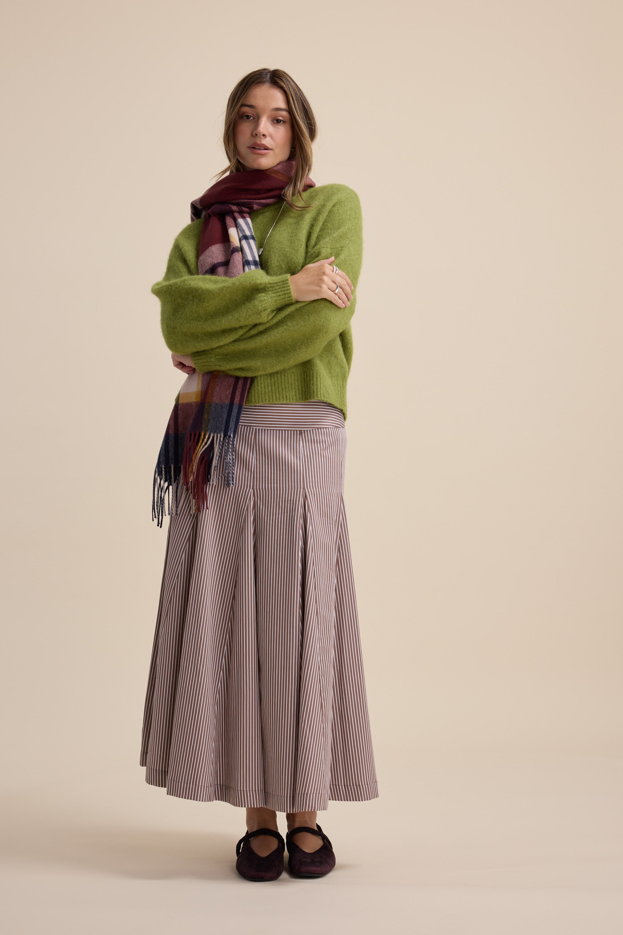 Woman in green sweater, plaid scarf, Max Marley Panel Seam Skirt, and dark shoes standing.