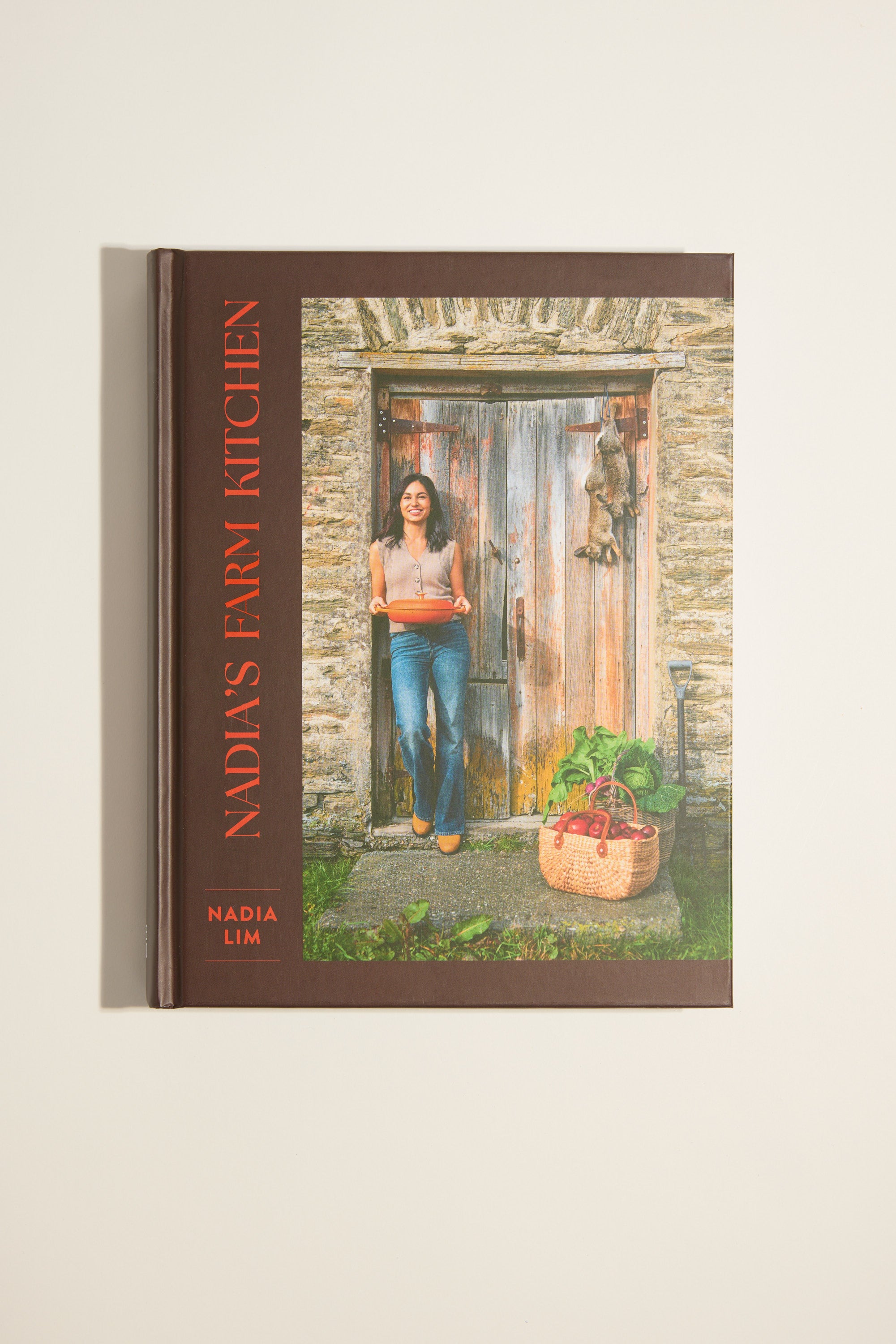 The Nadia's Farm Kitchen Book by Other showcases a woman at a rustic wooden door with vegetables, celebrating New Zealand farm life and fresh, seasonal recipes.
