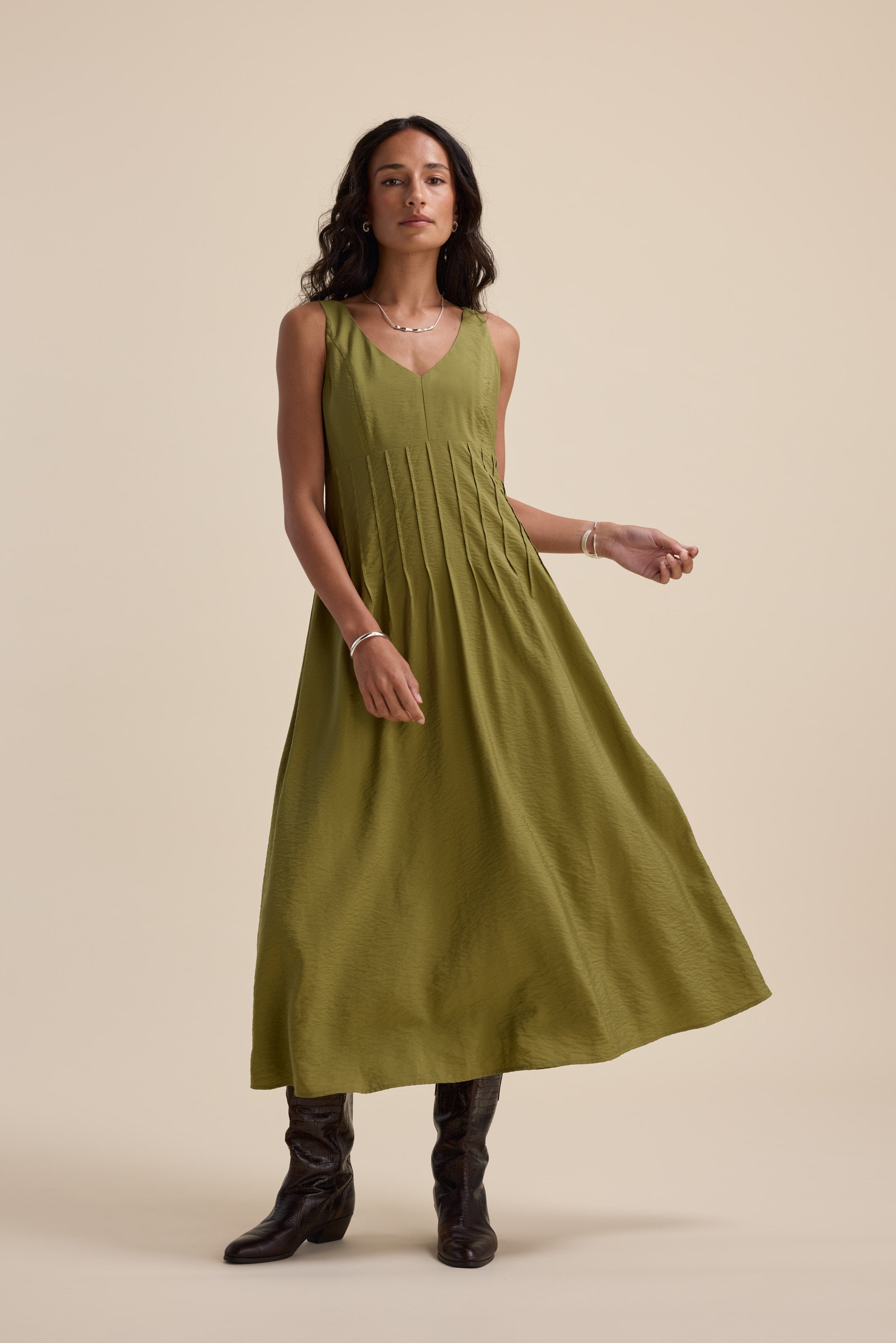 Woman in Max’s Nina Fit and Flare Dress in dill green with black boots, beige background.