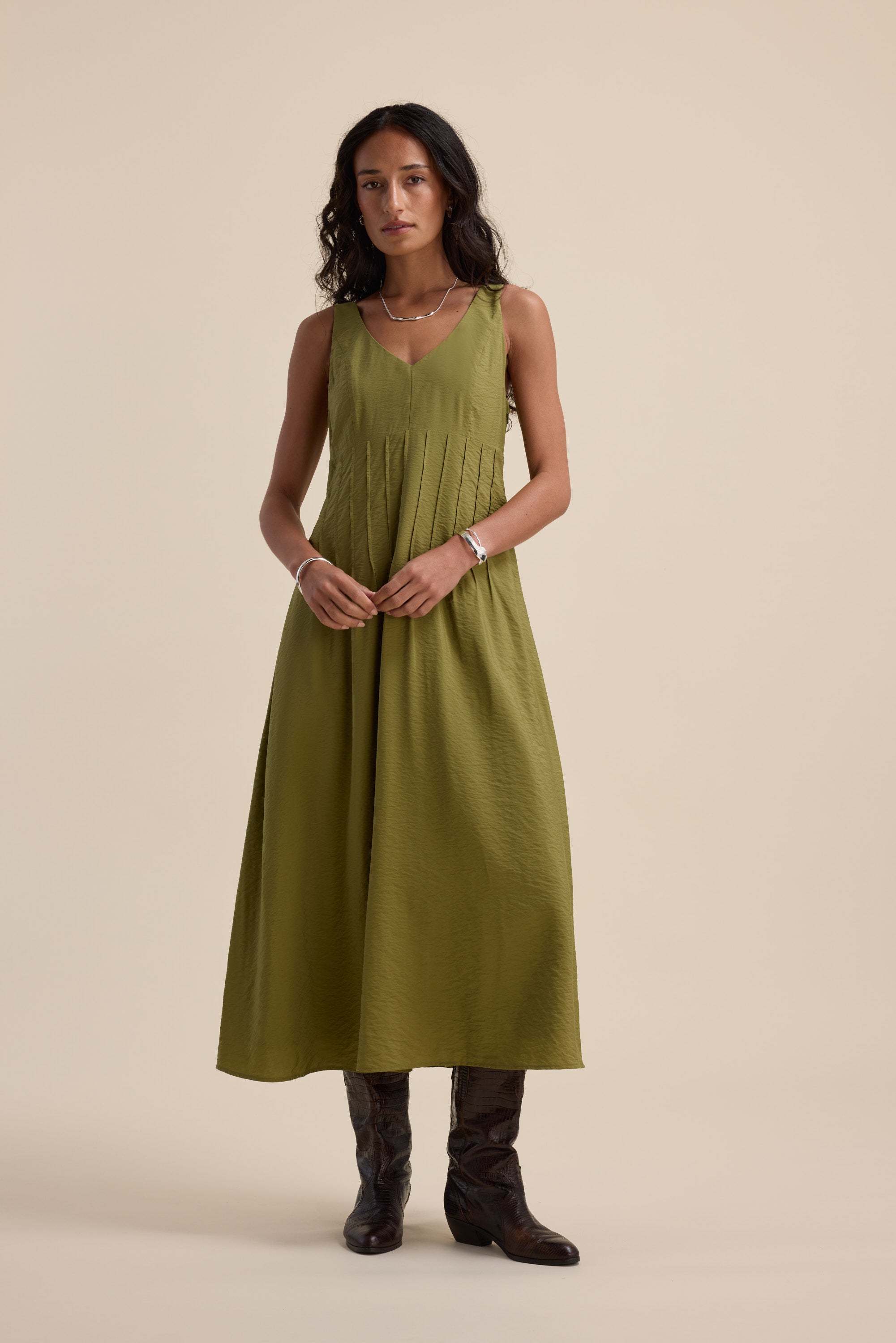 Woman in the Max Nina Fit and Flare Dress, dill green, with dark boots against a beige background.