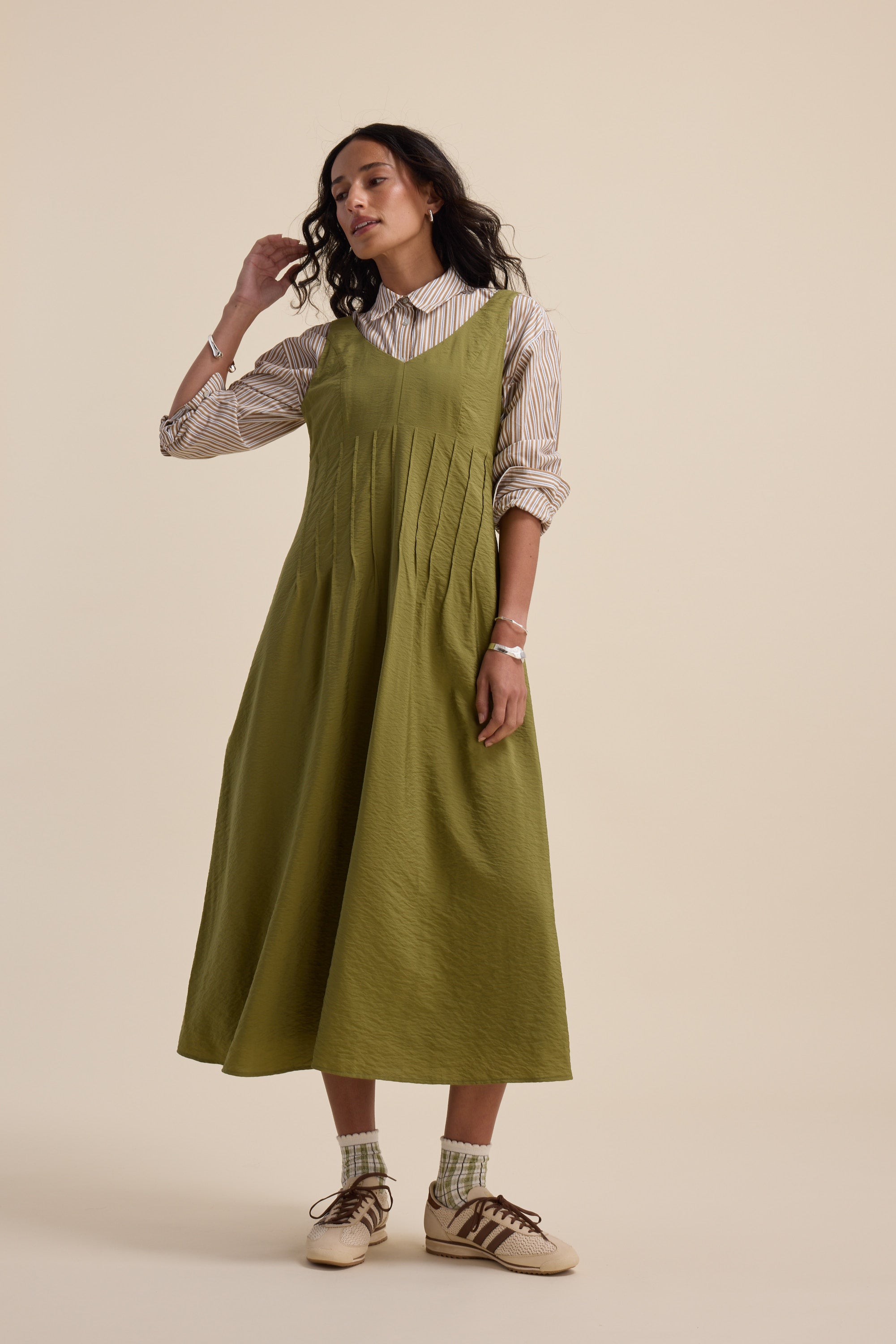 Woman in Max’s Nina Fit and Flare Dress in dill green over a striped shirt with socks and sneakers.