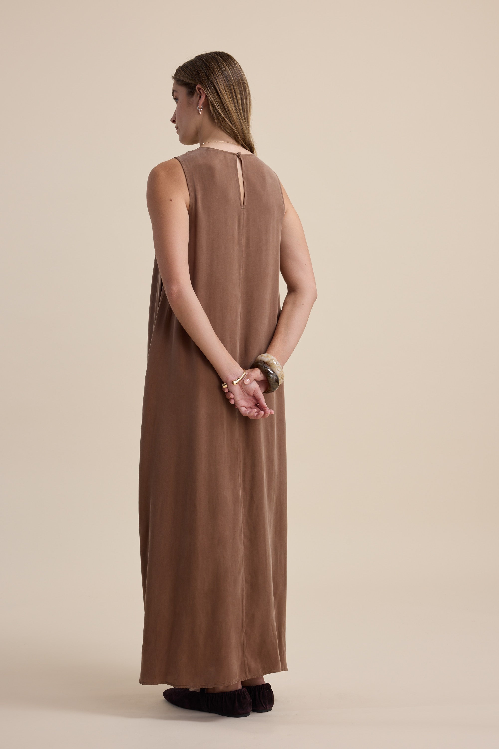 Woman in a sleeveless brown Kaitlyn Flared Midi Dress by Max stands with her back facing us.