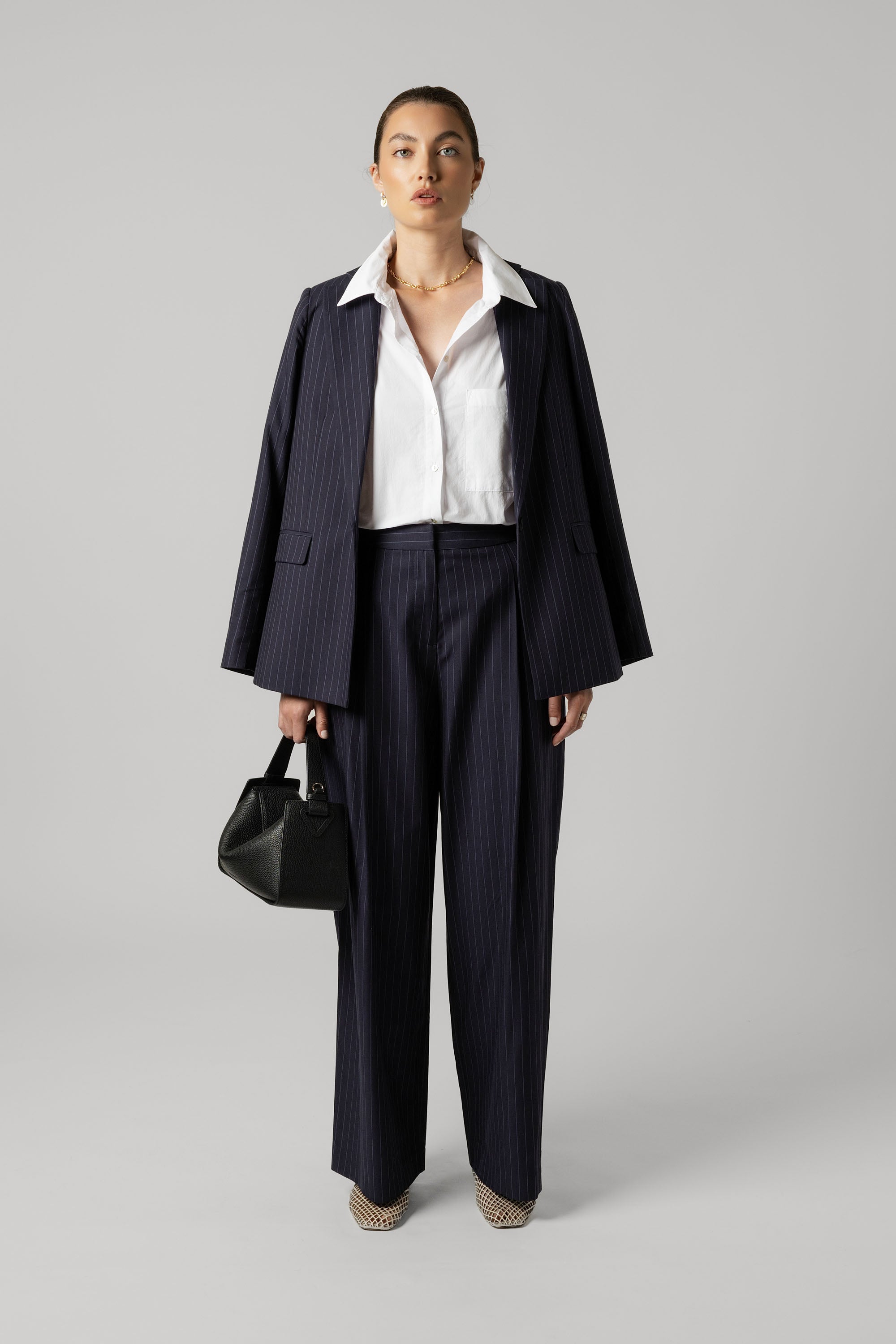 Woman in Max Everyday Tailored Shirt, holding a black handbag on gray background.