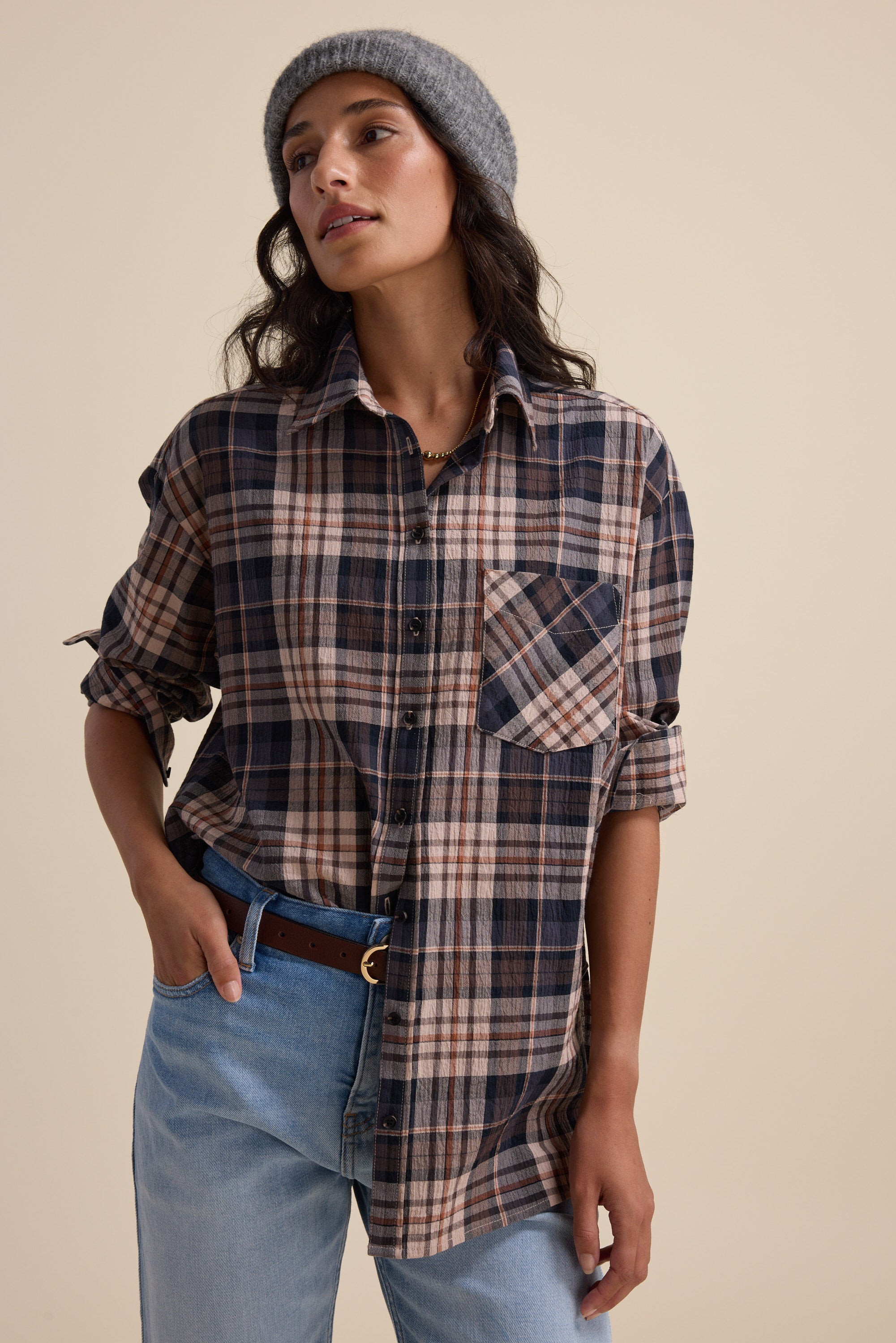 Woman in an Elementary Textured Shirt, light blue jeans, and gray beanie against a beige backdrop.
