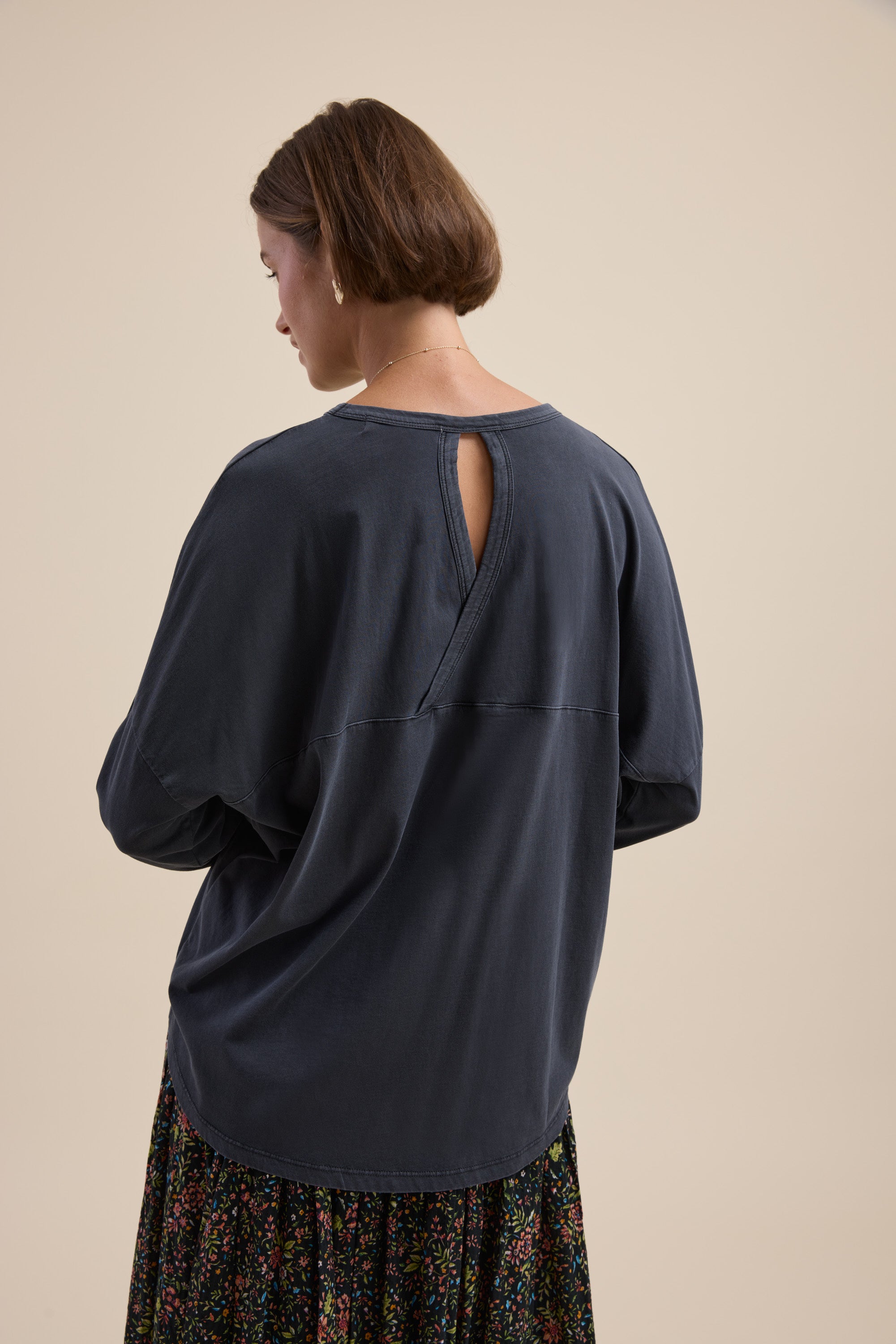 Woman with short hair in Max Elementary Slouchy Long Sleeve Tee, navy, floral skirt, back view.